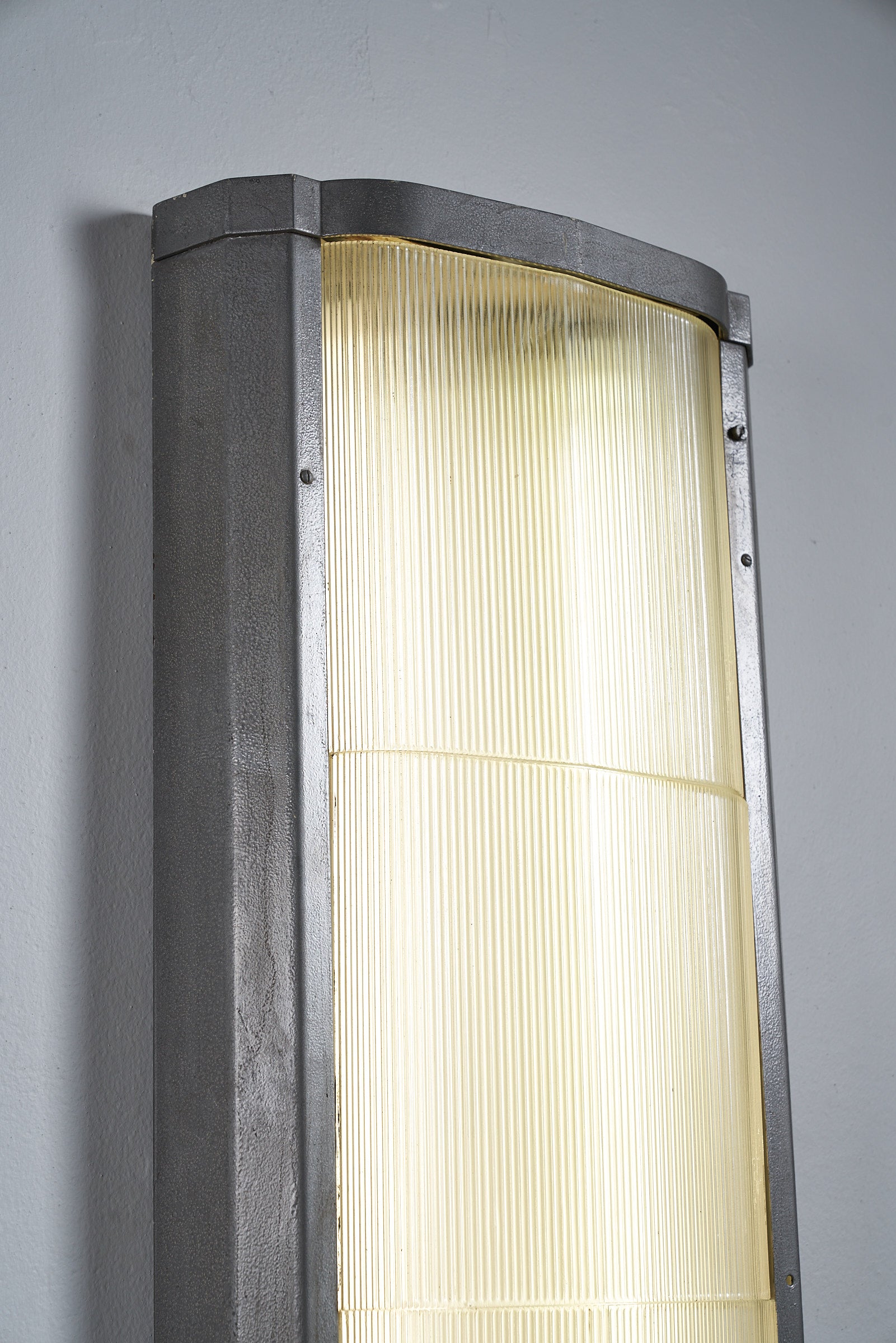 Industrial mount with glass diffuser emitting soft light against a grey wall