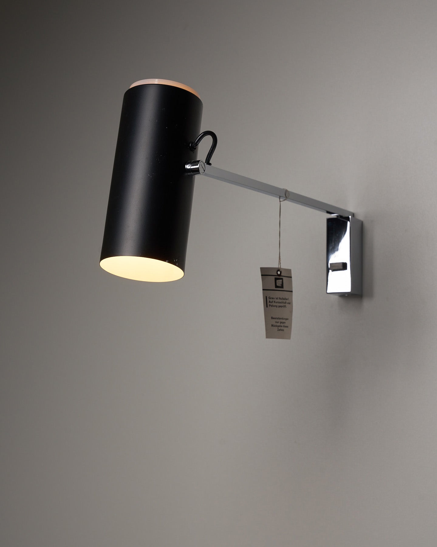 Directional Wall Spot by Cosack Leuchten with chrome mount, adjustable arm, and black pivoting cylindrical shade emitting soft, diffused light.