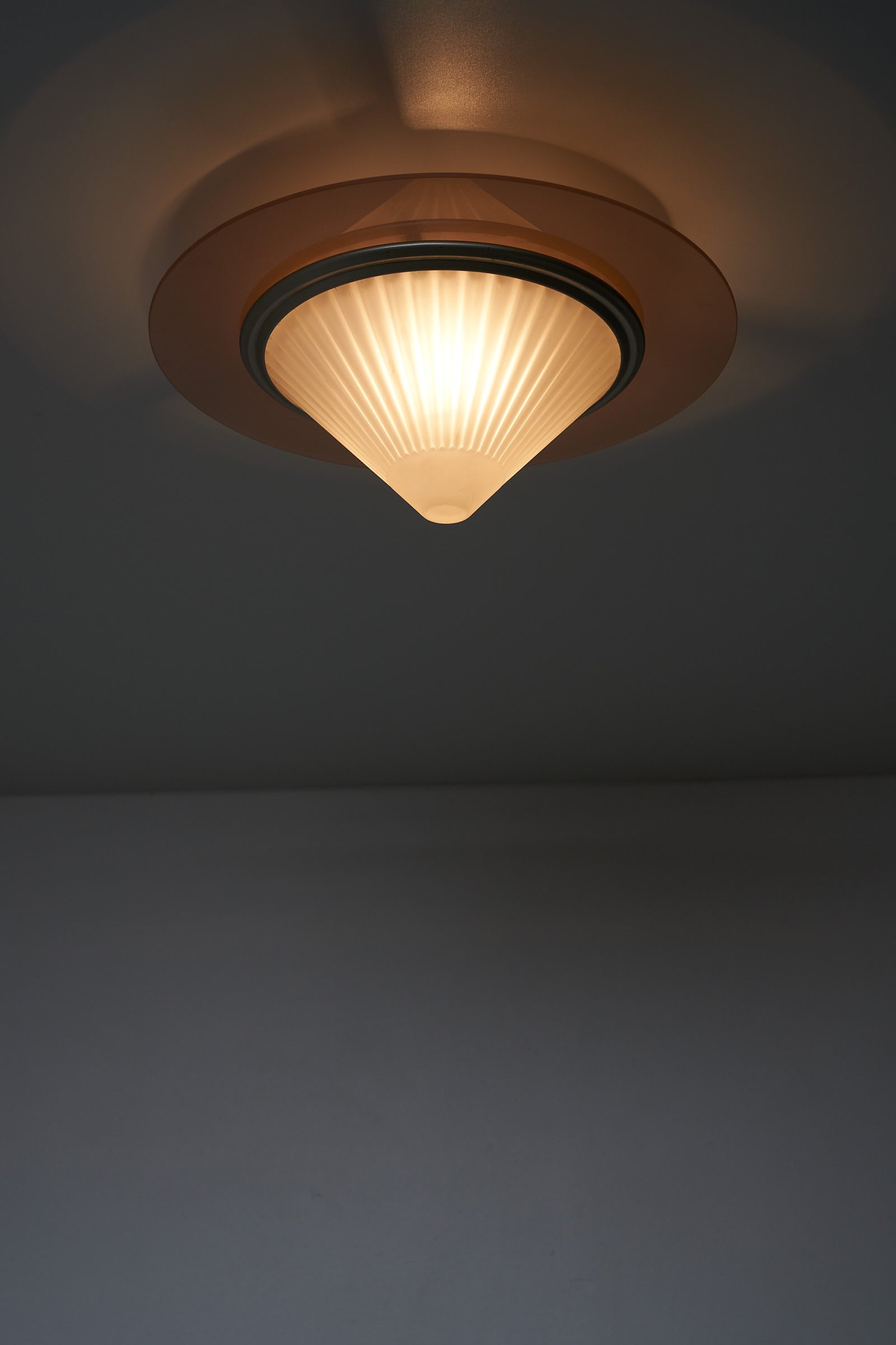 images of the Atena Ceiling Lamp by Ezio Didone for Arteluce, Italy, 1980s. The lamp features a frosted glass cone-shaped diffuser with a colored glass ring around it, separated by a brass ring. The design includes a metal frame that creates a distance between the glass element and the ceiling, producing a backglow effect. The lamp retains its original sticker.