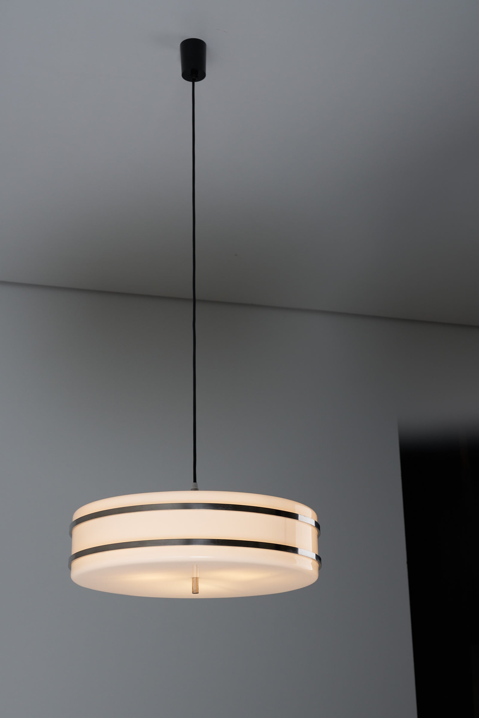 Circular pendant light by Stilux Milano with a flat cylindrical plexiglass form, chromed steel accents, and a repainted black exterior.