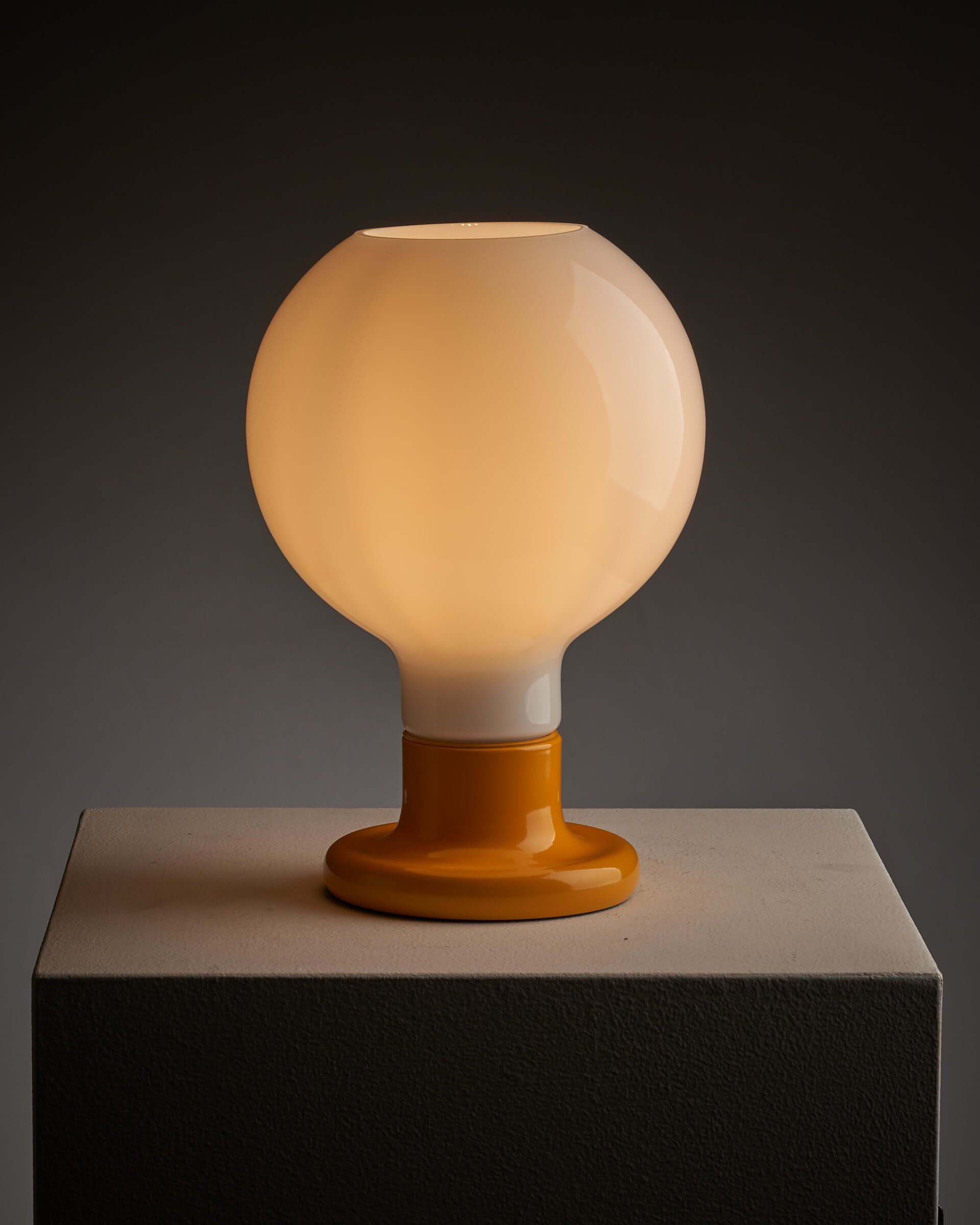 Yellow lacquered table lamp with milk glass sphere glowing warmly, perfect for modern, classical, or eclectic interiors.