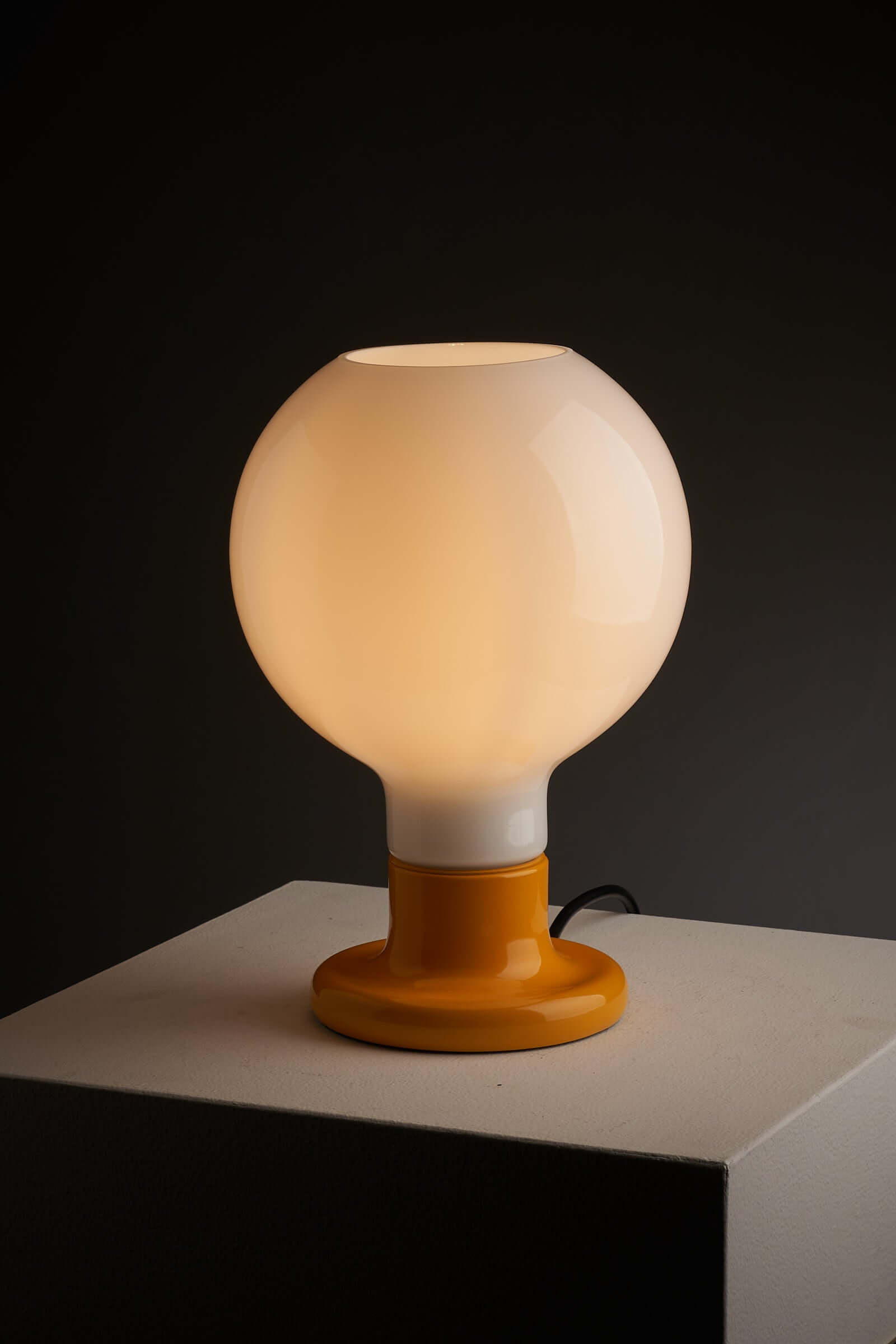 Cosack Leuchten table lamp with yellow lacquered base and glowing milk glass sphere on a pedestal against dark background.