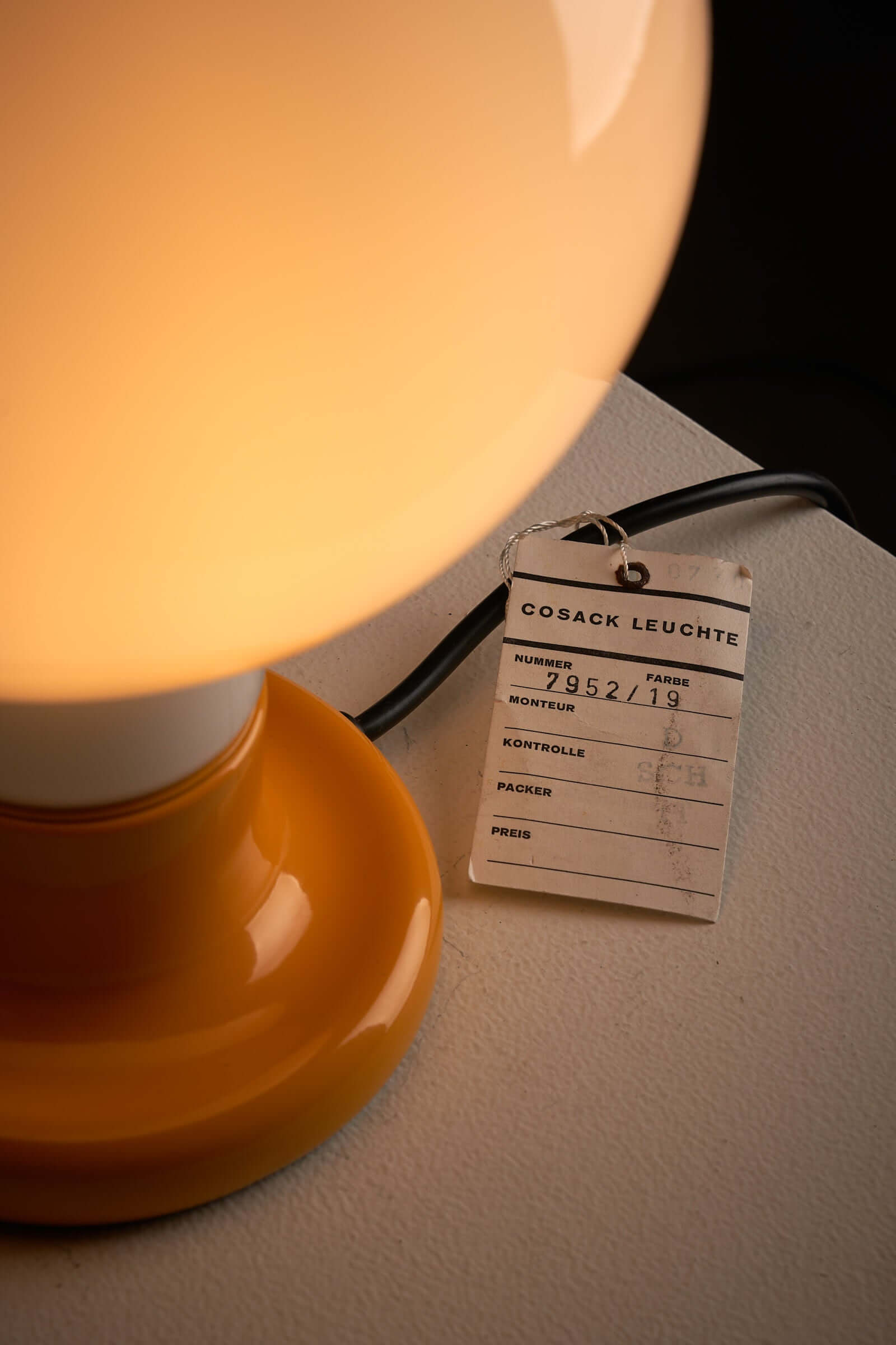 Cosack Leuchten table lamp with glowing milk glass sphere and yellow lacquered base on display with manufacturer tag.