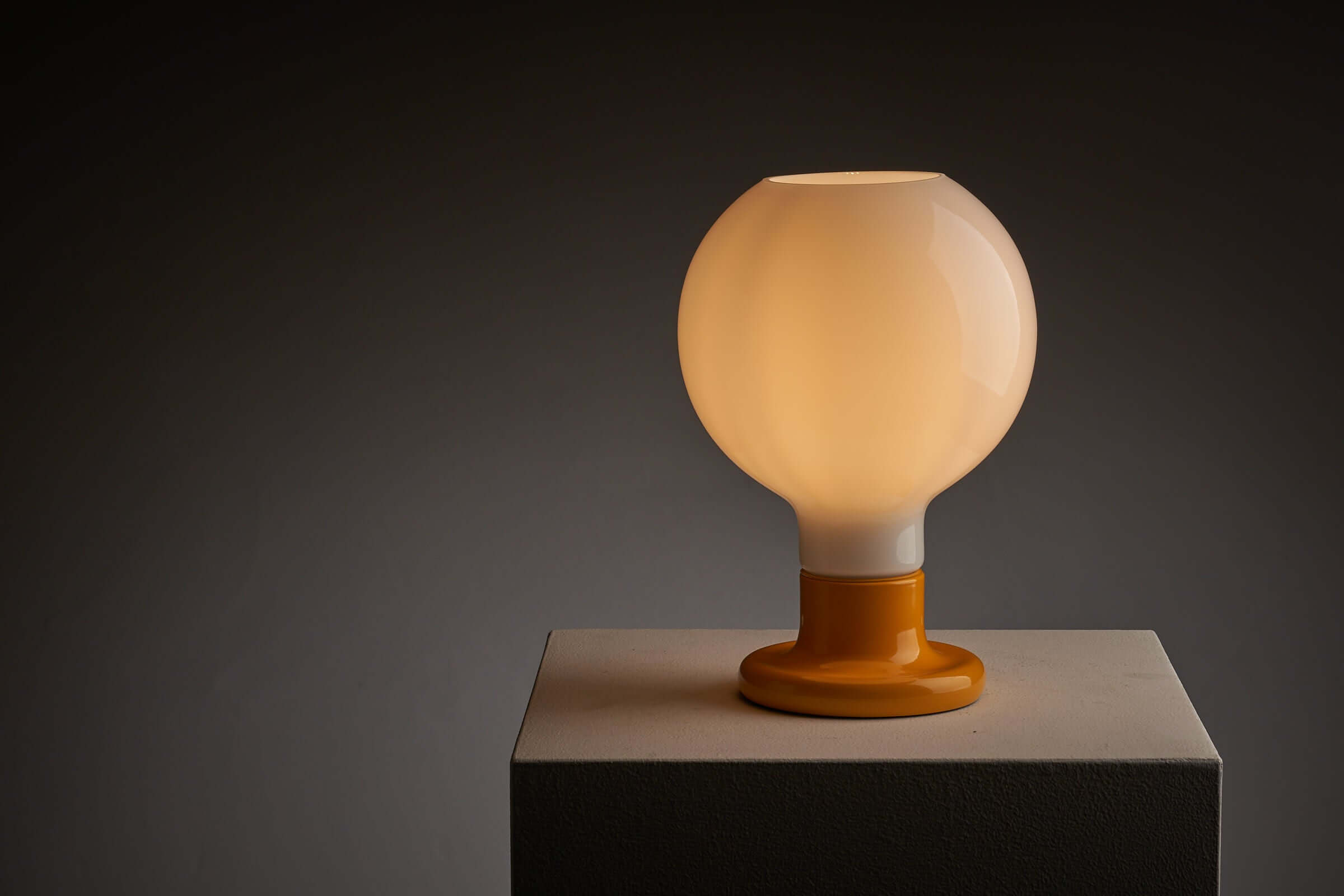 Yellow lacquered base table lamp with glowing milk glass sphere, combining modern and classical design for a warm and welcoming atmosphere.