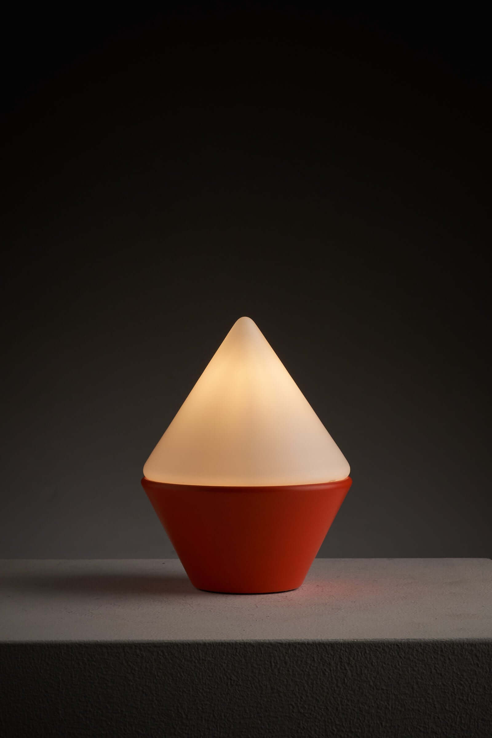 Cosack Leuchten table lamp with orange base and triangular opal glass shade, casting a warm glow on a minimalist surface.