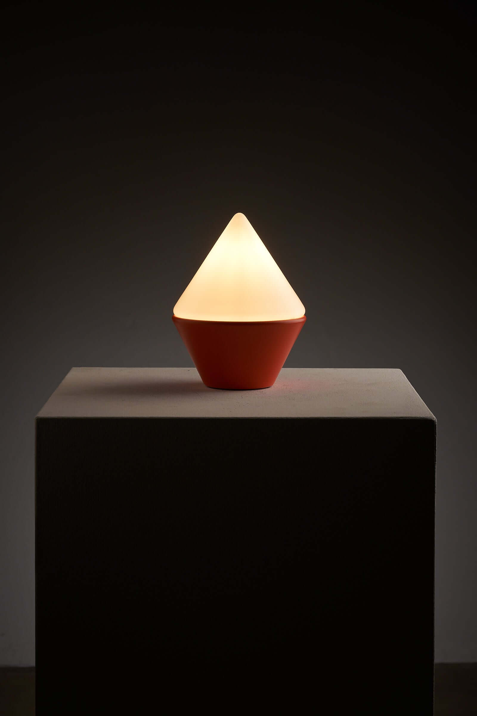 Cosack Leuchten table lamp with vibrant orange base and triangular opal glass shade on a pedestal, glowing softly.