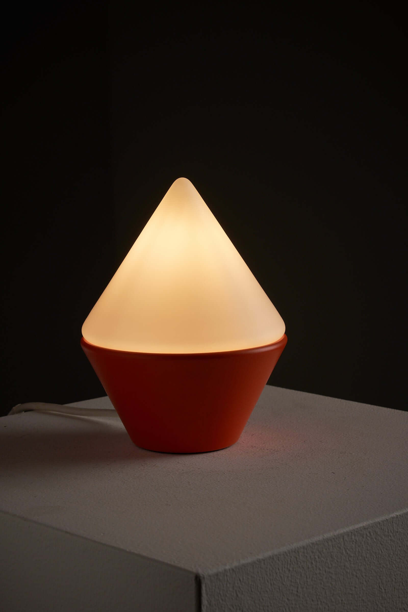 Cosack Leuchten table lamp with orange base and triangular opal glass shade illuminating a dark setting.