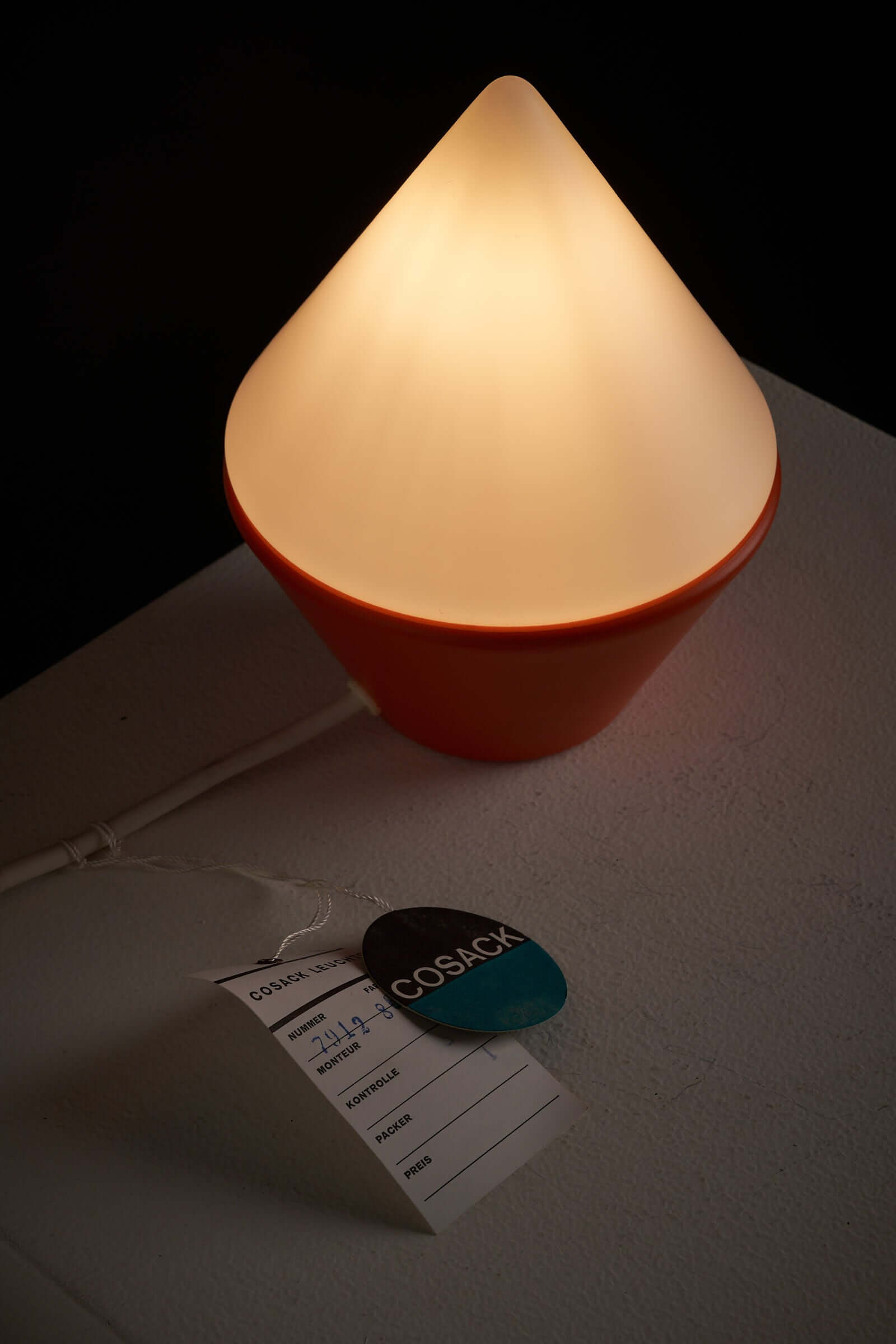 Cosack Leuchten table lamp featuring triangular opal glass shade and vibrant orange base on display with tags.