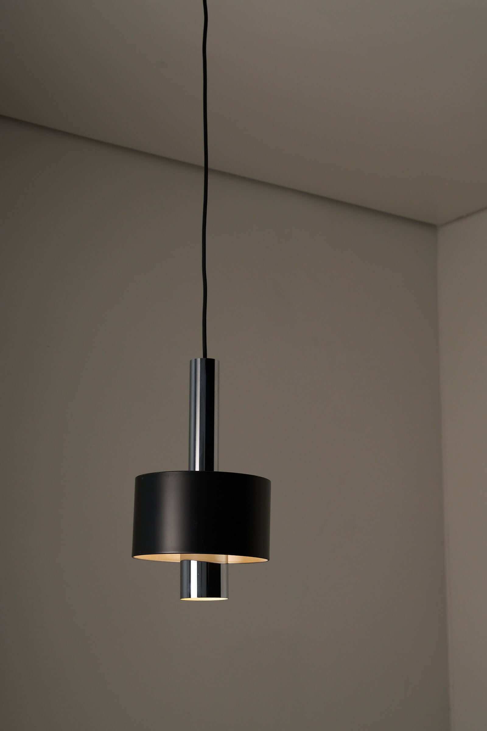 Black pendant lamp with chrome inner frame illuminating a minimalist room.