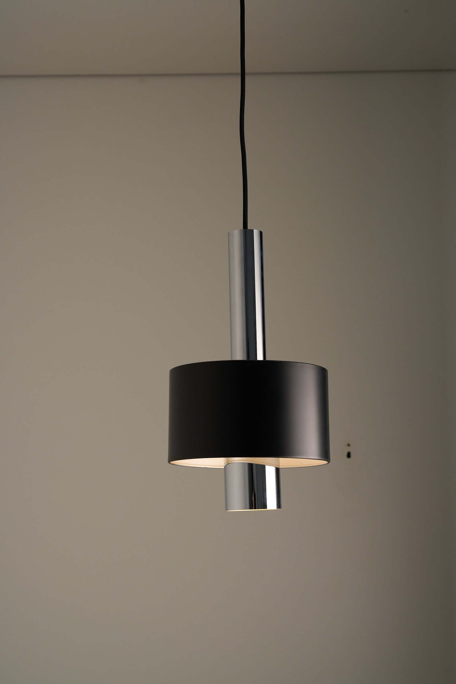 Black pendant lamp with polished chrome inner frame and matte black diffuser in minimalist mid-century design.