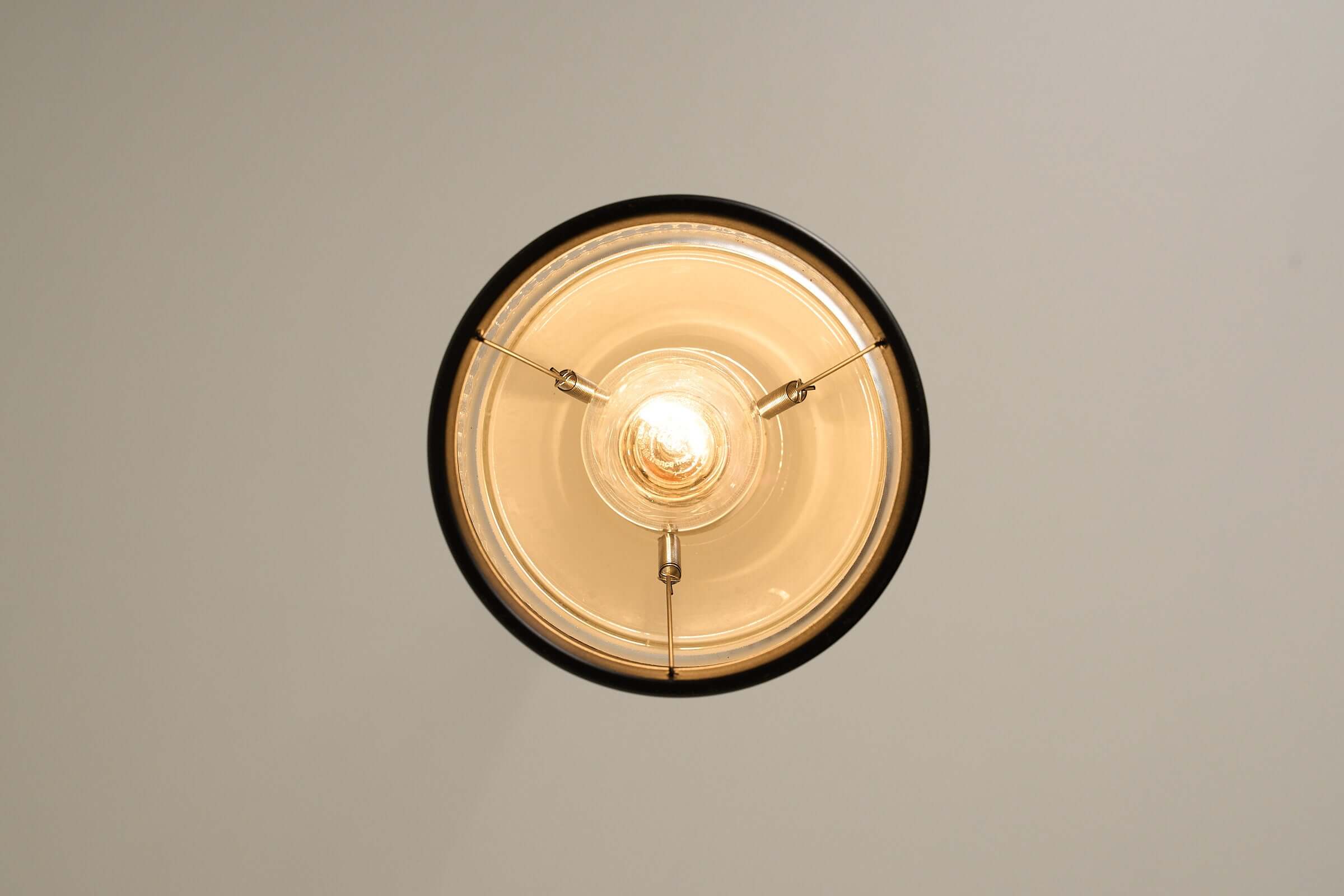 Black pendant lamp with textured glass and innovative spring connection viewed from below.