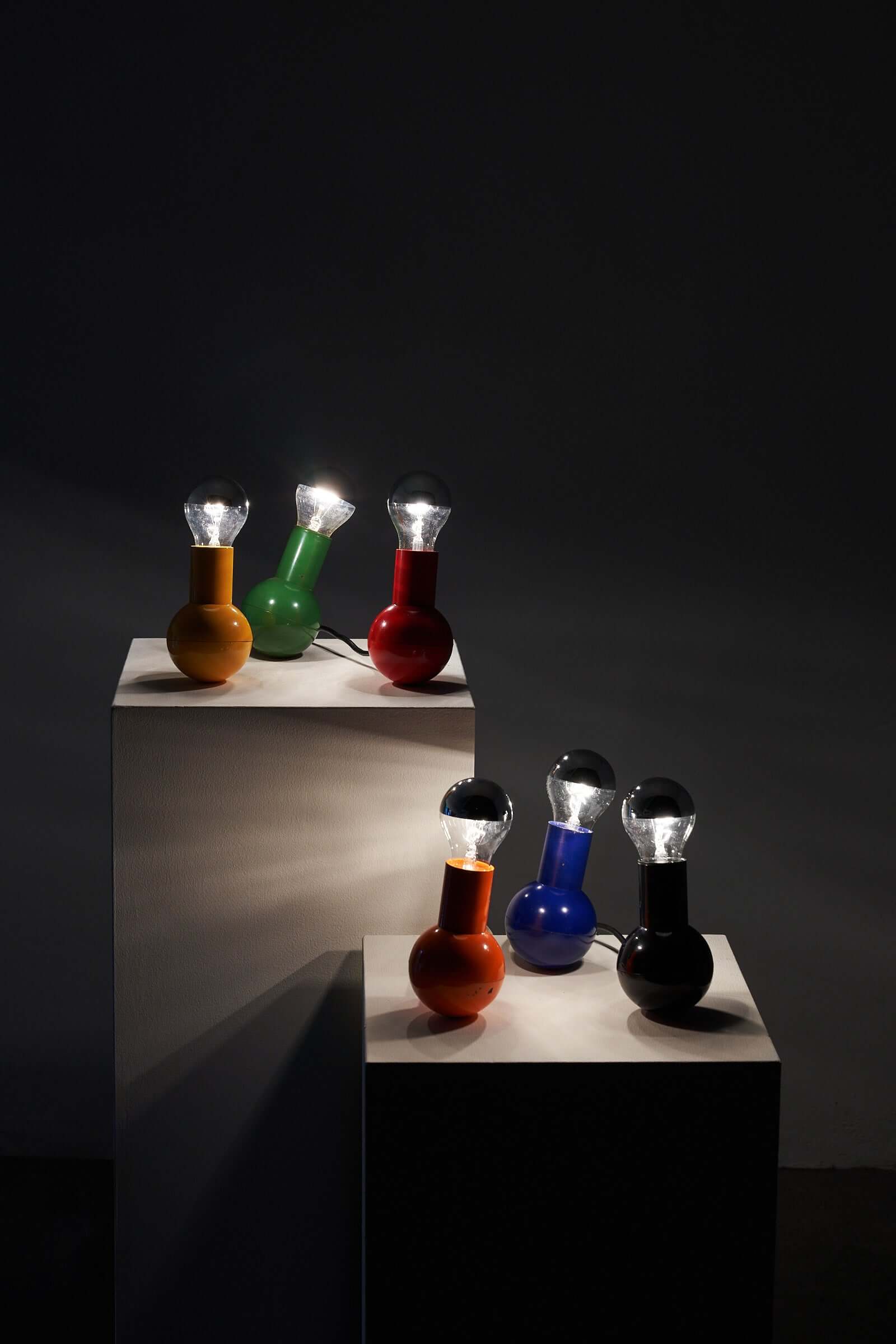 Various vibrant Kugel Table Lamps by Cosack Leuchten displayed on white pedestals in a dark room.