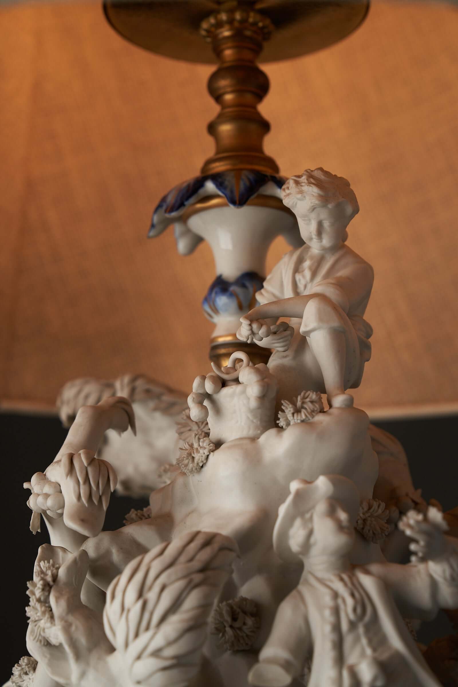 Porcelain table lamp with sculpted figurines by Mangani, featuring intricate high relief biscuit porcelain figures on a cobalt blue base.