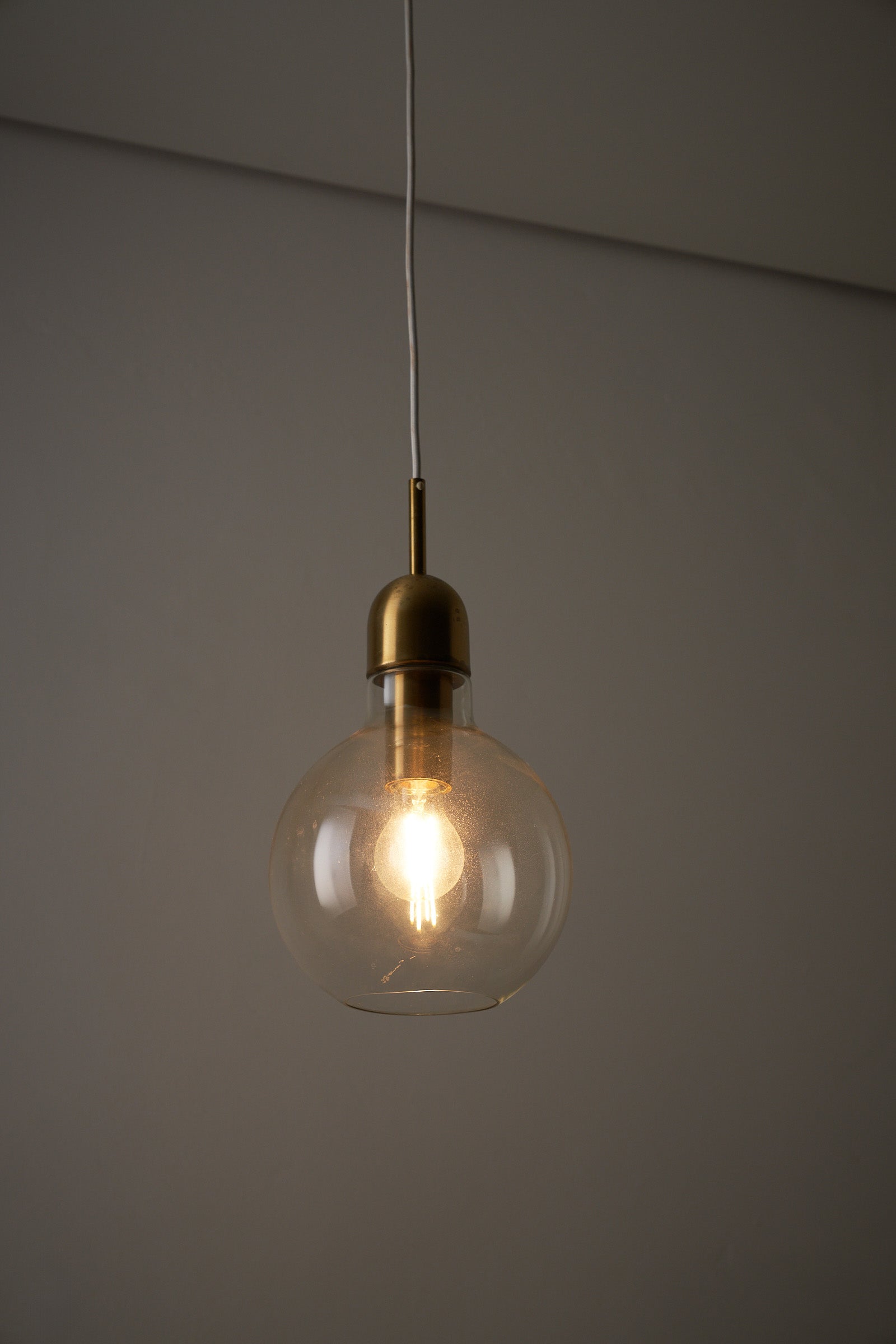 Brass and clear glass pendant light with glowing bulb, showcasing minimalist and mid-century design for modern interiors.