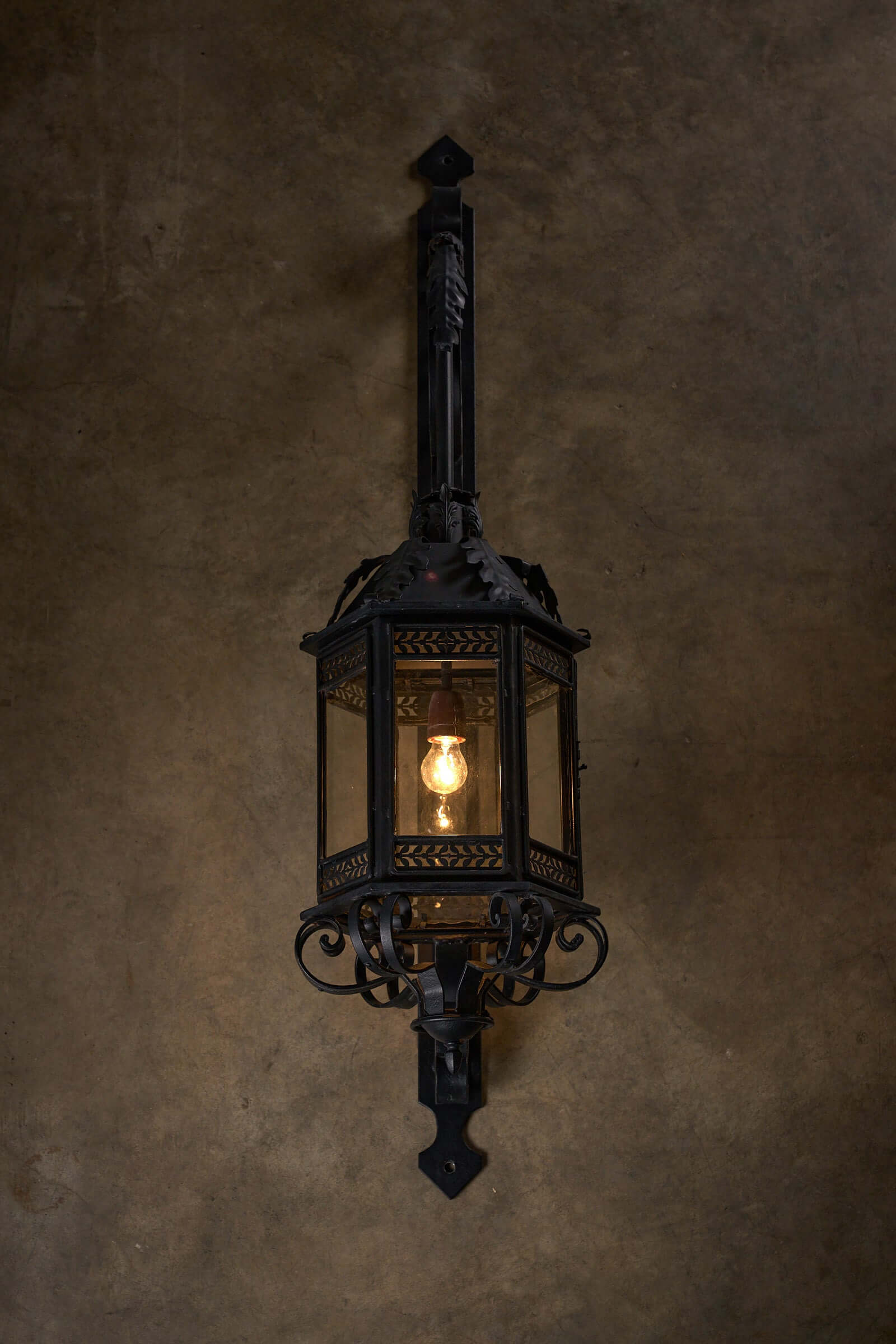 Antique XL wrought iron wall lantern with intricate scroll designs, illuminated.