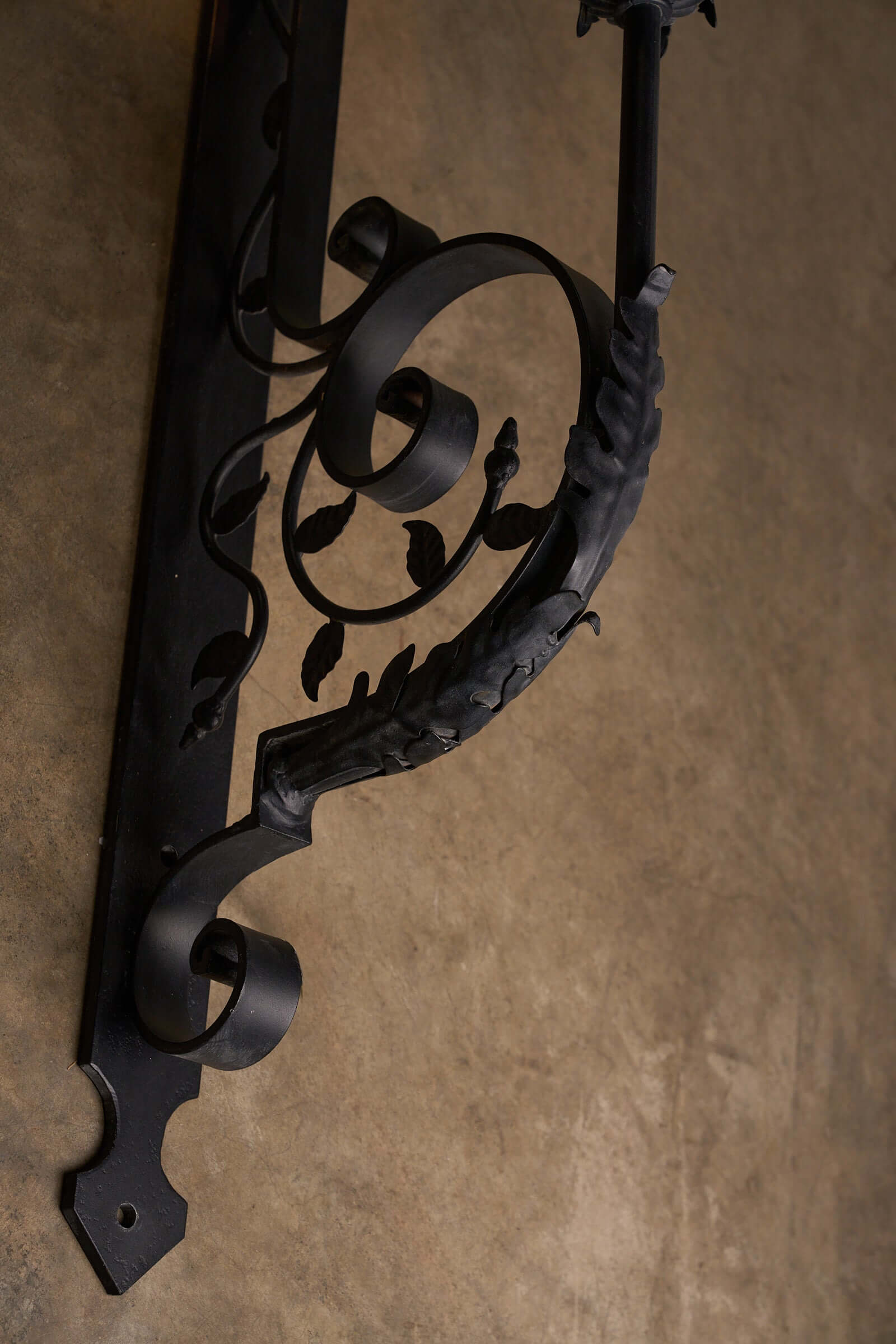 Antique wrought iron wall lantern with intricate scroll designs and leaves, shown from a side angle.