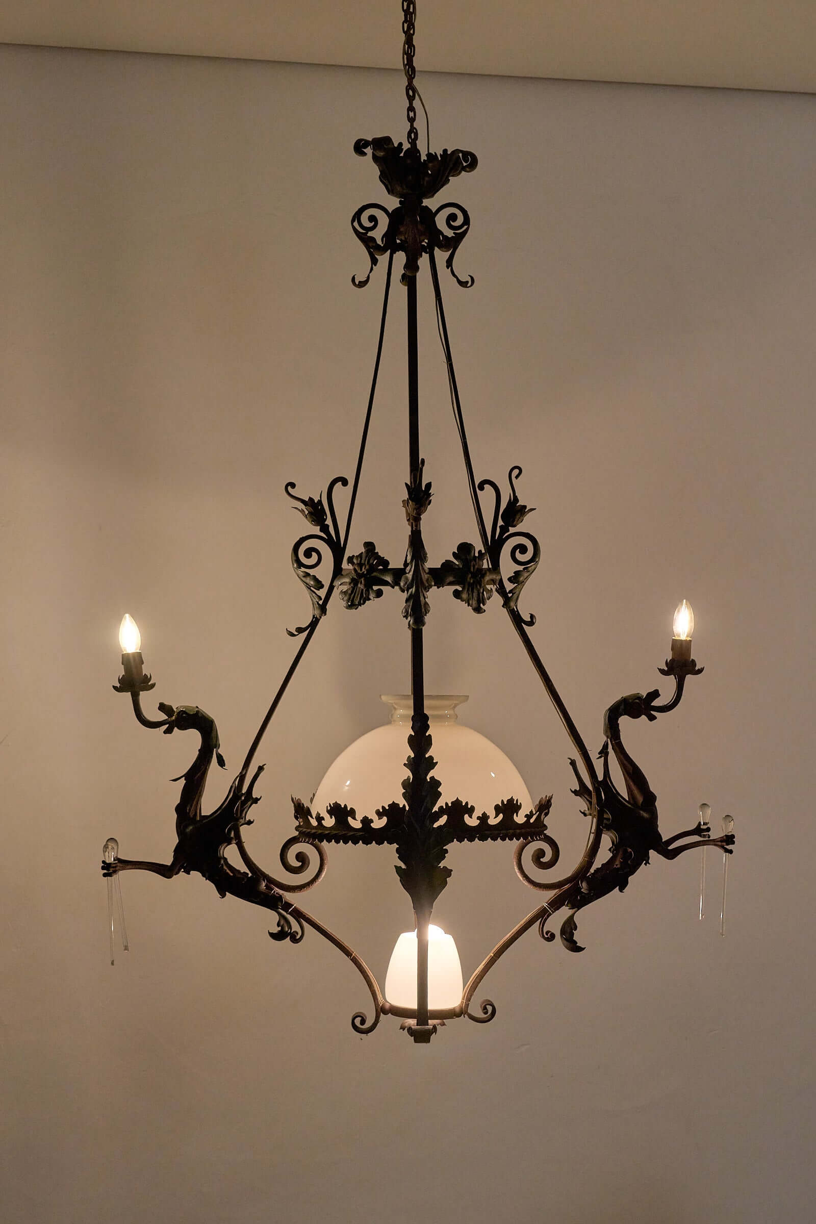 Antique iron chandelier with dragons and central glass shade, showcasing gothic and vintage charm for classic interiors.