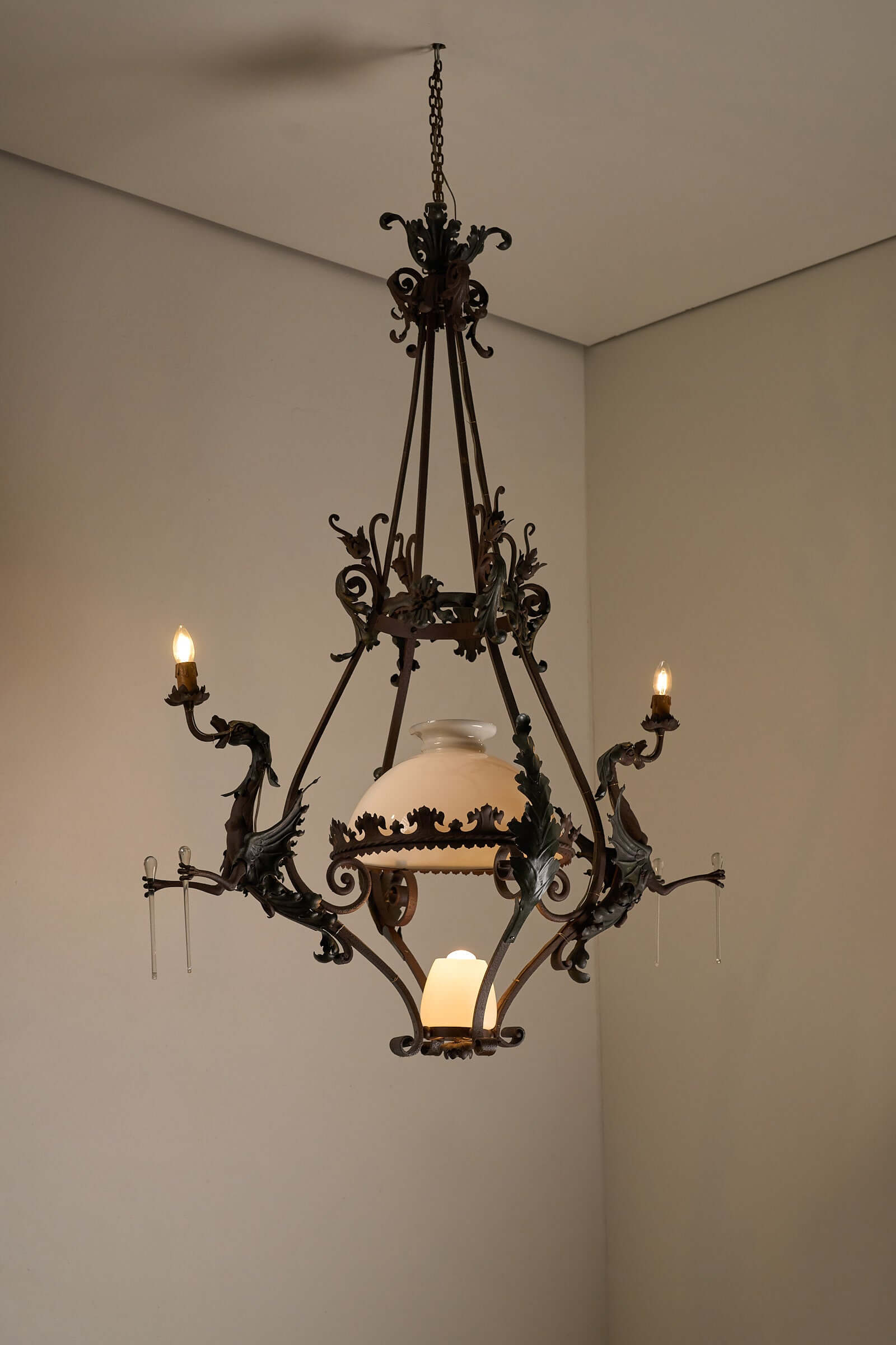 Antique iron chandelier with dragon figures, showcasing gothic designs and a vintage glass shade for ambient lighting in classic interiors.