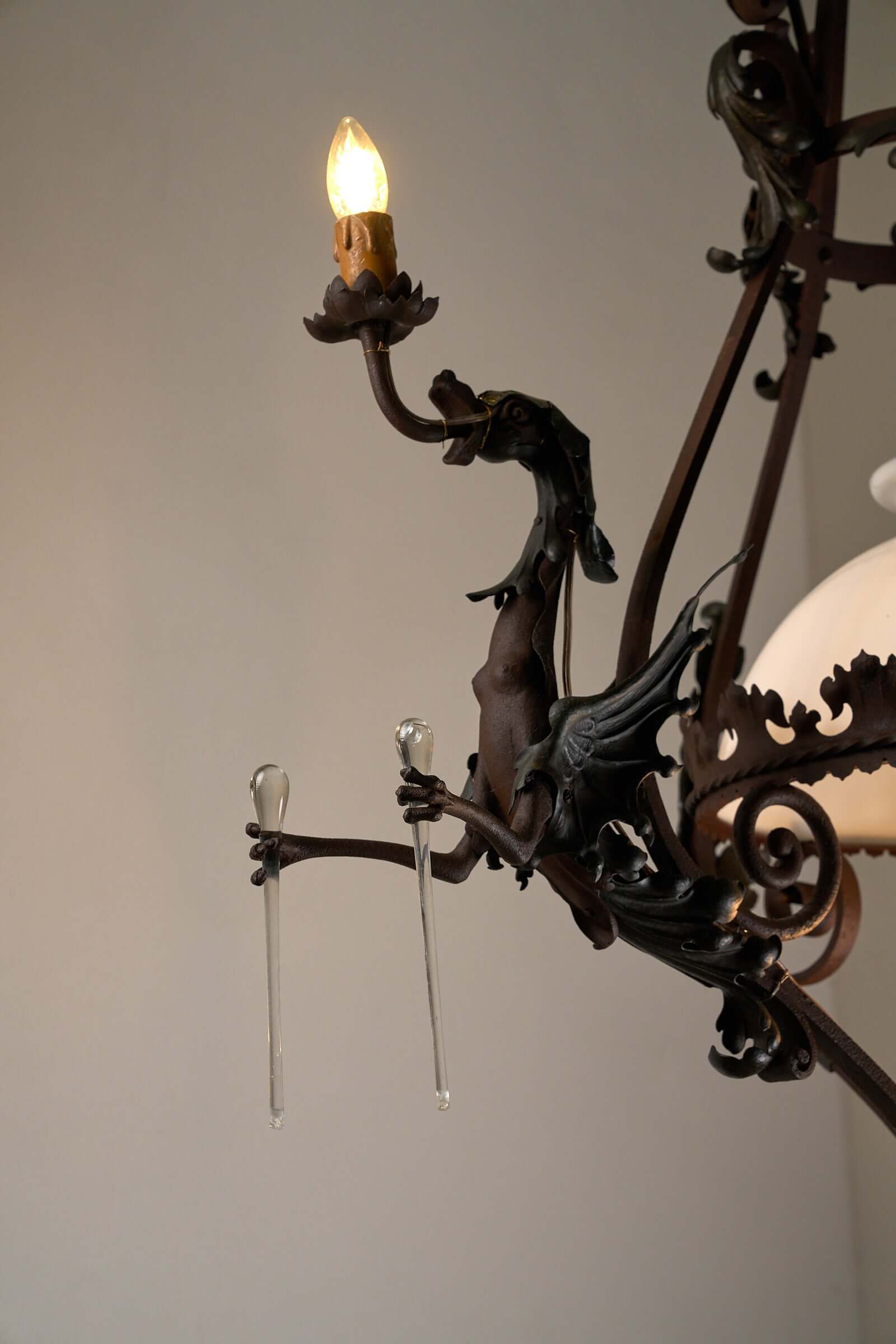 Antique iron chandelier with intricate dragon figure and warm light, blending gothic and vintage aesthetics for classic interiors.