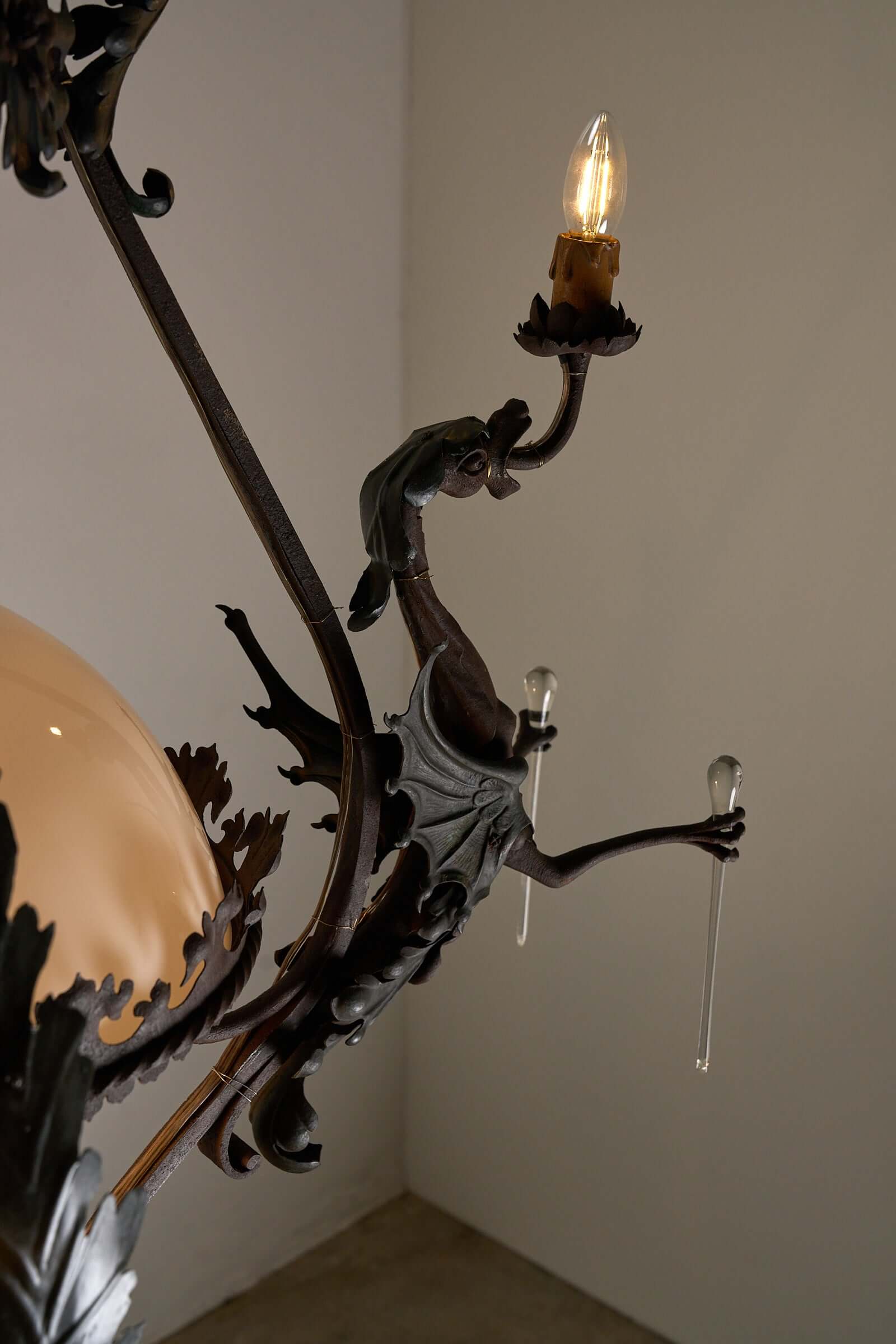 Antique iron chandelier with dragon figure and glowing bulb, showcasing gothic and vintage charm for eclectic interiors.