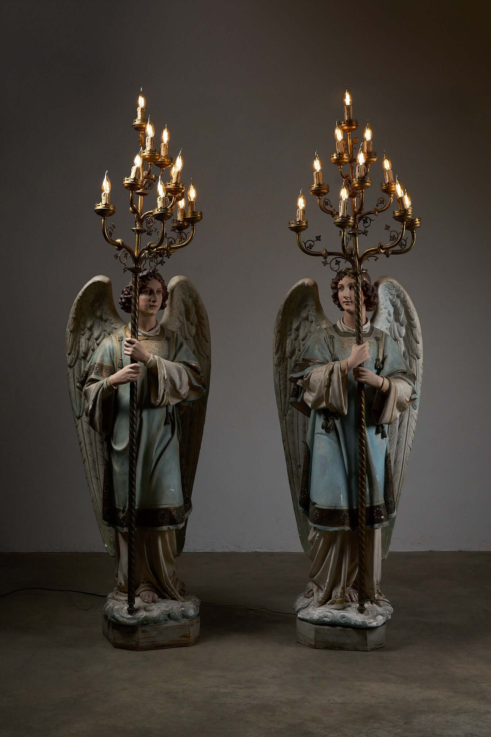 Antique 19th-century church angel candle holders with brass chandeliers, modified with electric lights, showcasing religious artistry.