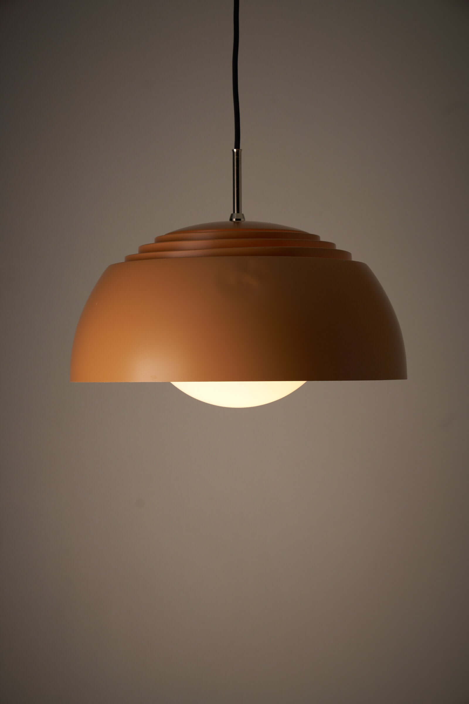 Pendant lamp with orange dome shade and opal glass diffuser, creating layered illumination.