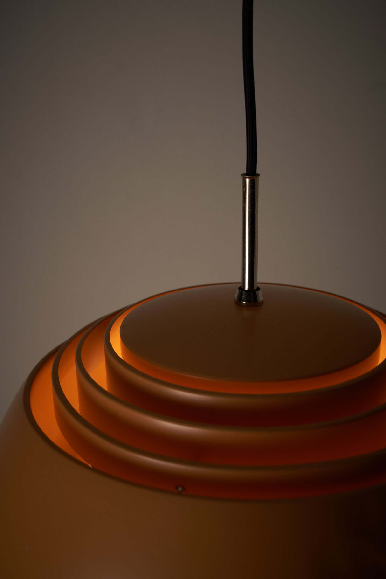 Close-up of B+L Leuchten pendant lamp with orange dome shade and subtle upward light diffusion.