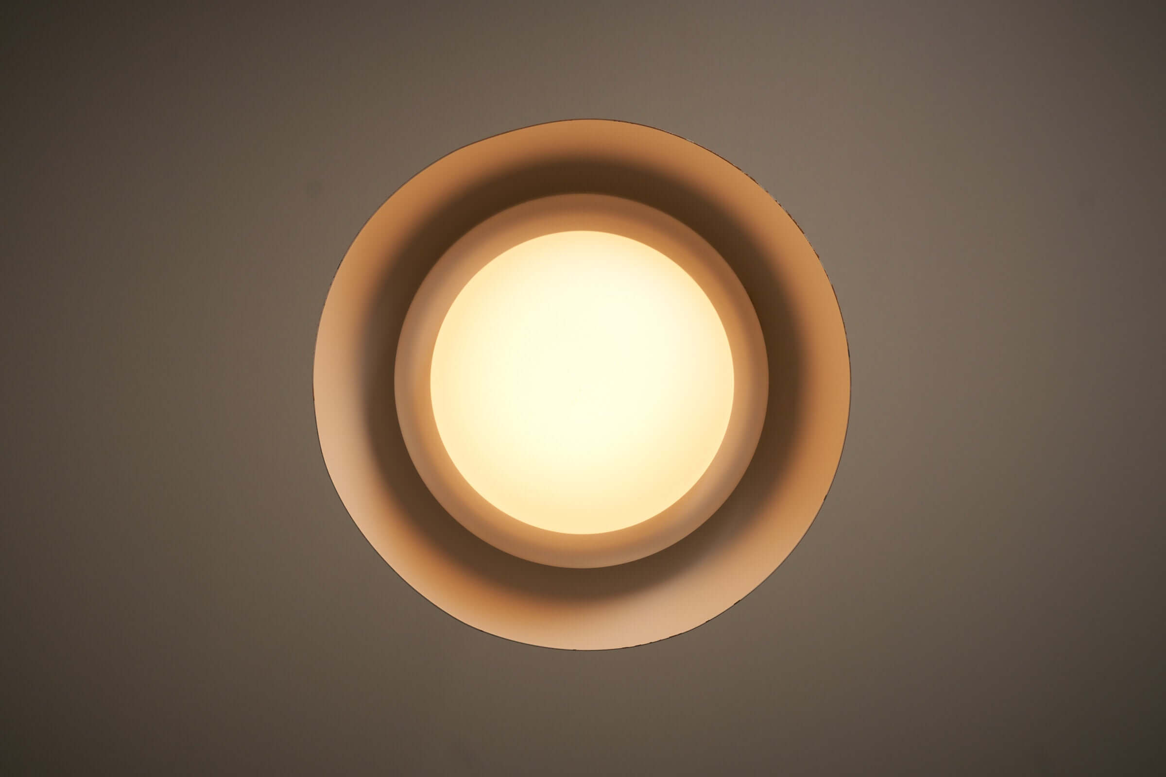 Pendant lamp with an orange dome shade and opal glass diffuser, viewed from below, highlighting layered light effect.