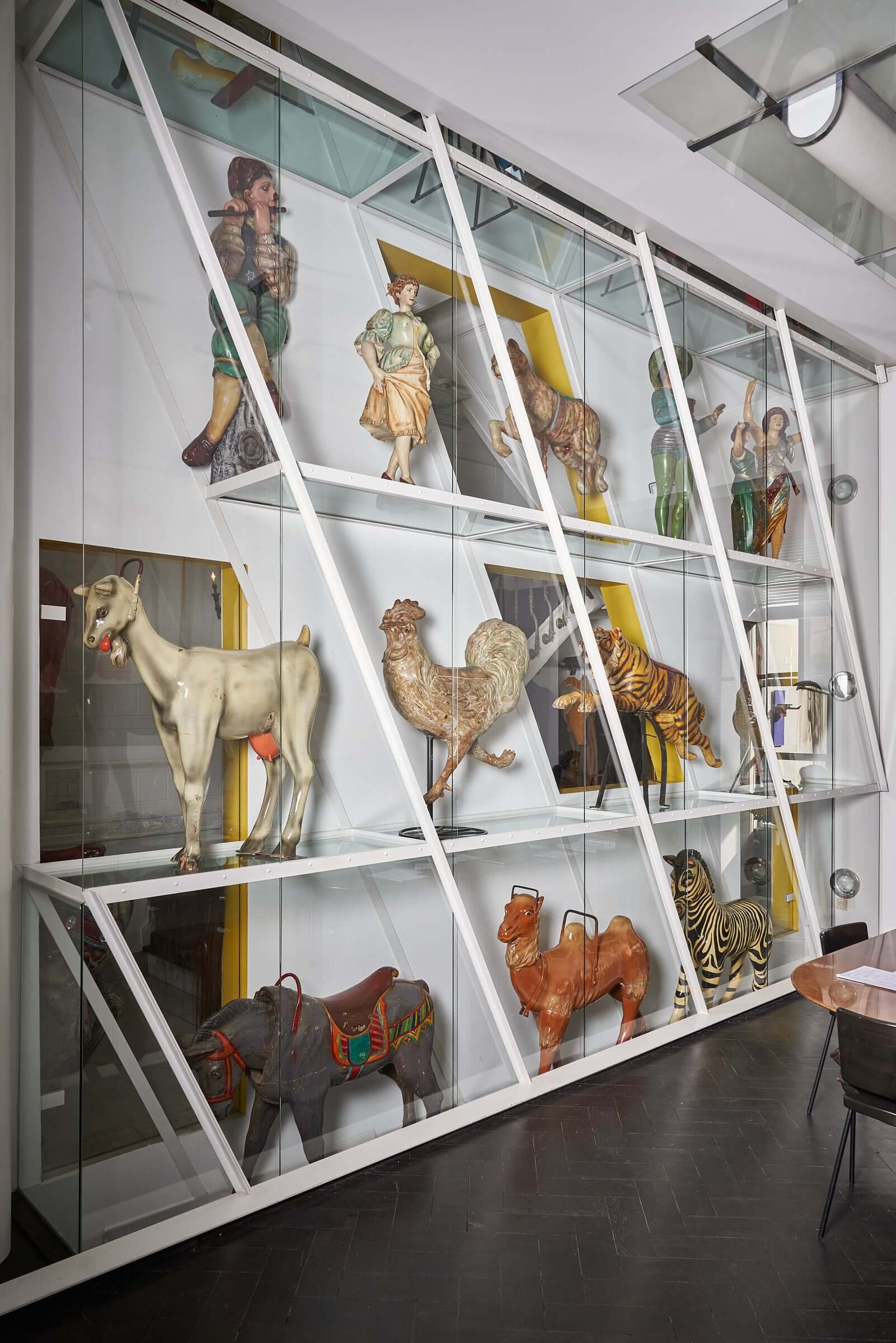 Antique wooden carousel figures of animals and characters displayed in a glass case.