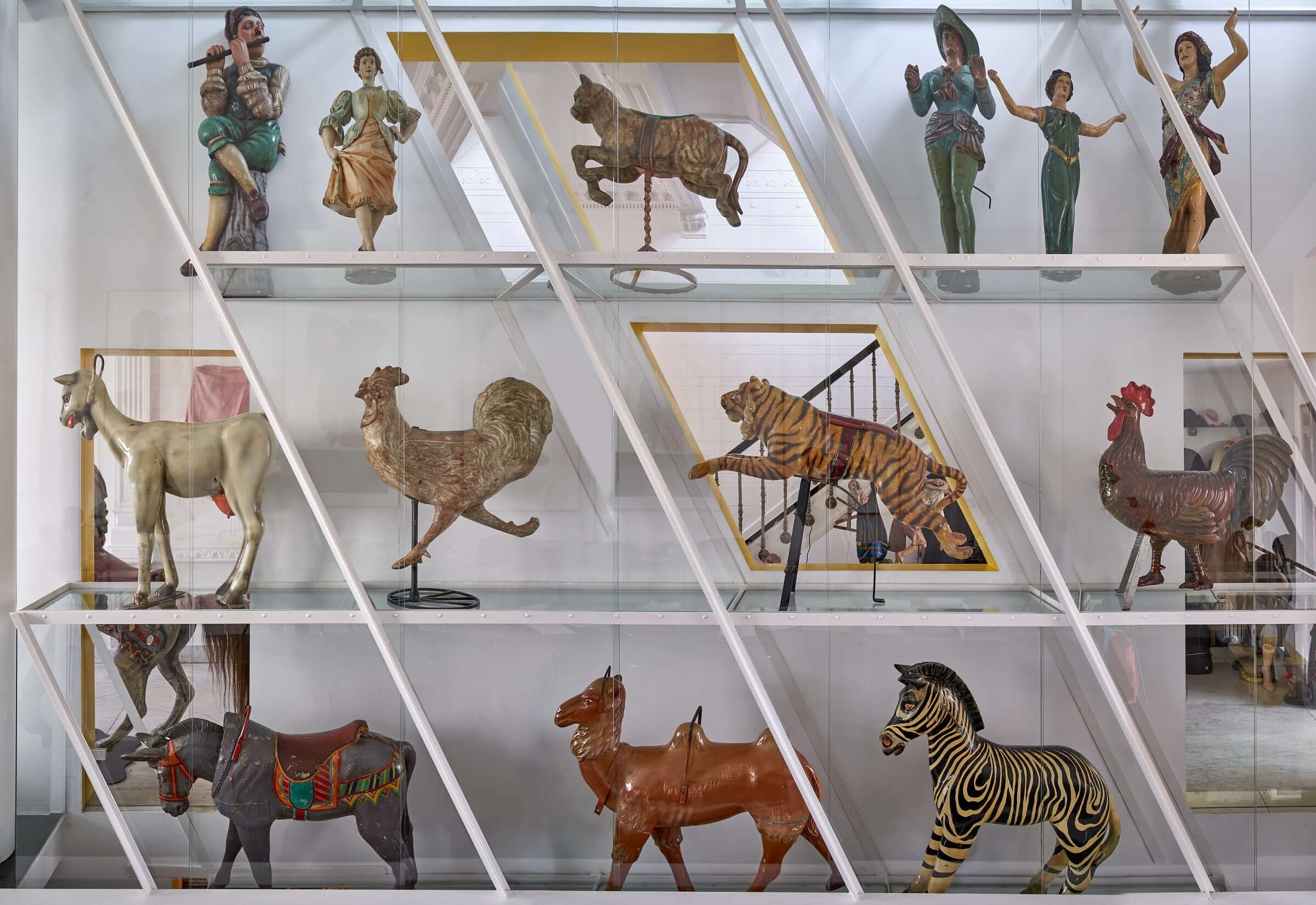 Antique wooden carousel figures display featuring animals and characters including a horse, rooster, tiger, and human figures.