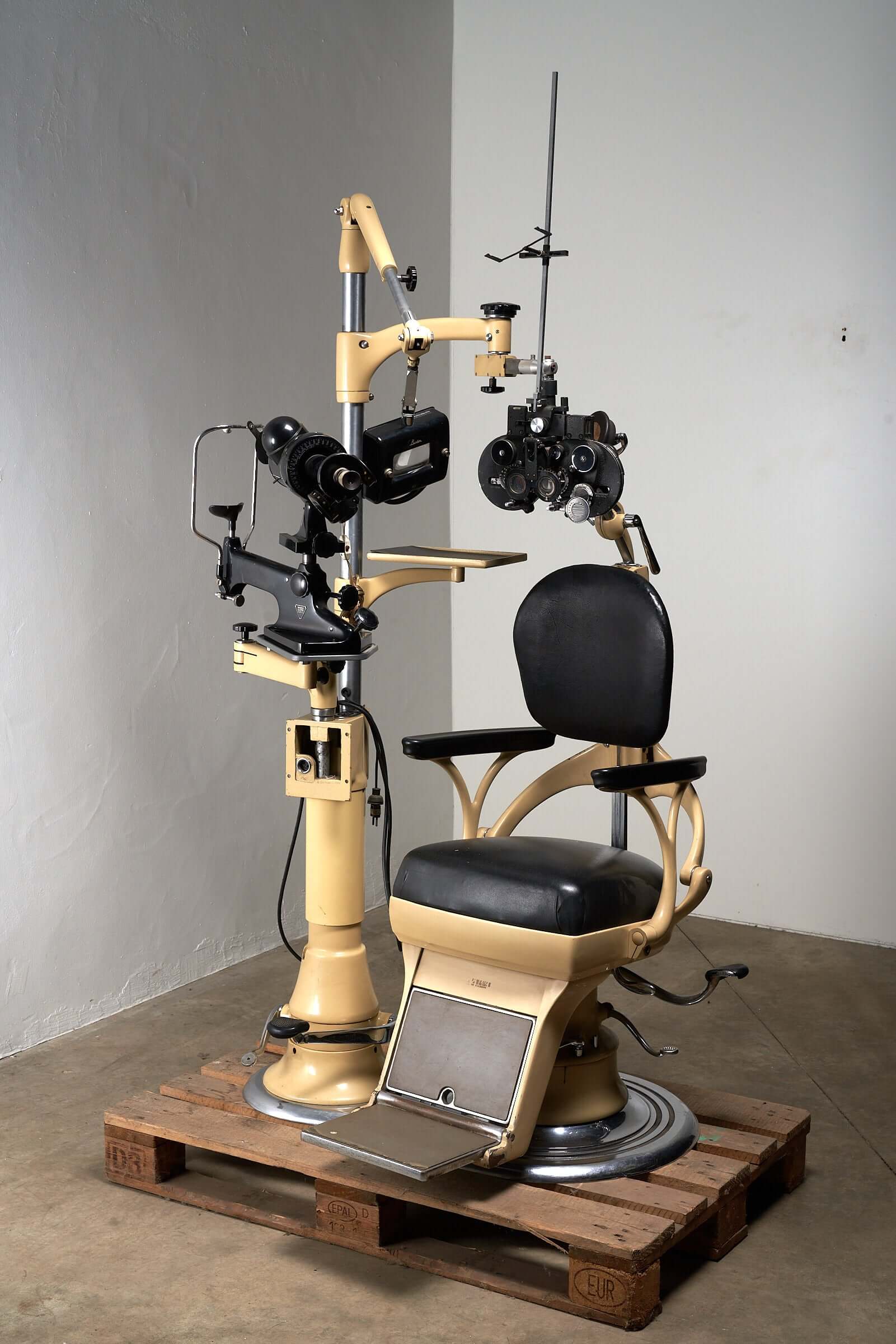 Vintage 1950s optometry examination chair and equipment with black leather upholstery and beige metal frame.