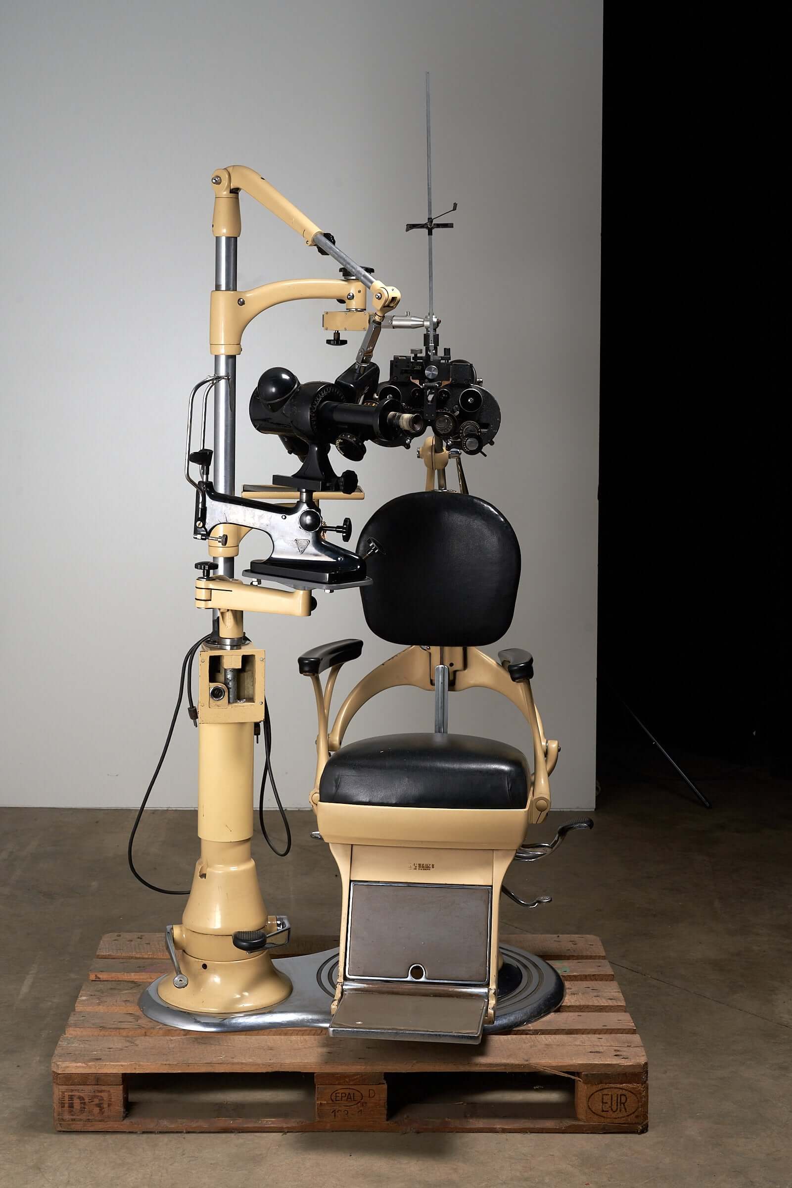 Vintage 1950s optometry examination chair and equipment with black leather upholstery and beige metal frame.