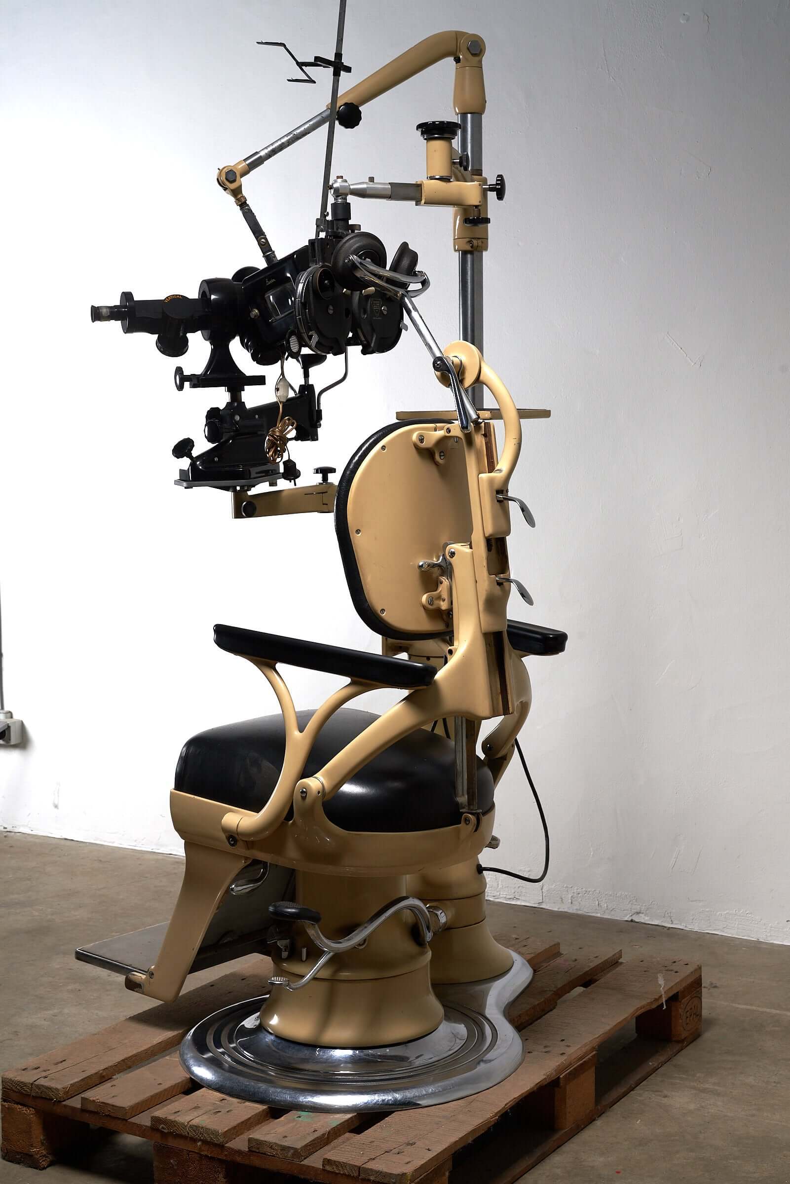 Vintage 1950s optometry examination chair with black leather upholstery and optometric instruments, beige metal frame