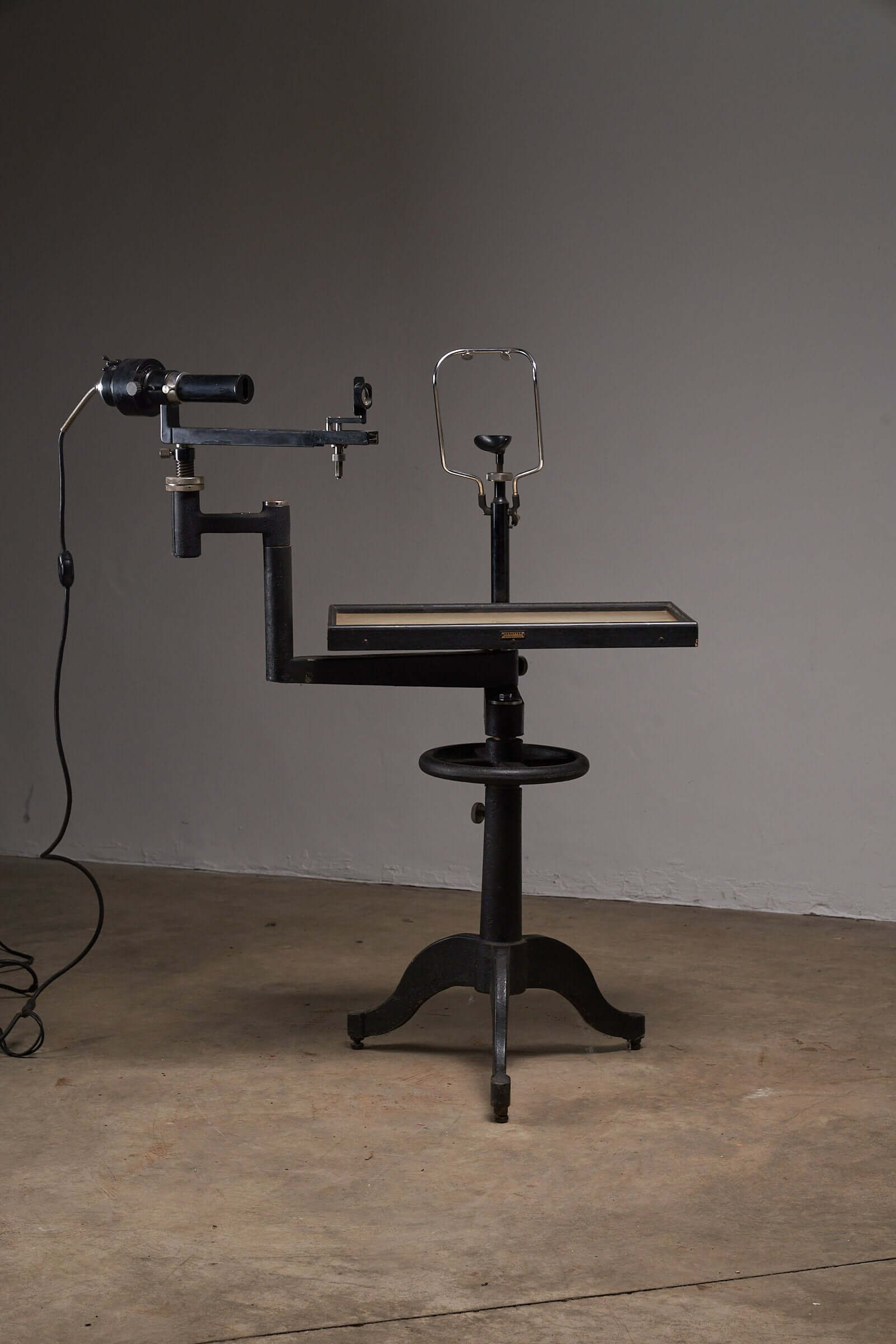 Vintage black optometry examination table from early 20th century with adjustable mechanism and industrial design aesthetic.