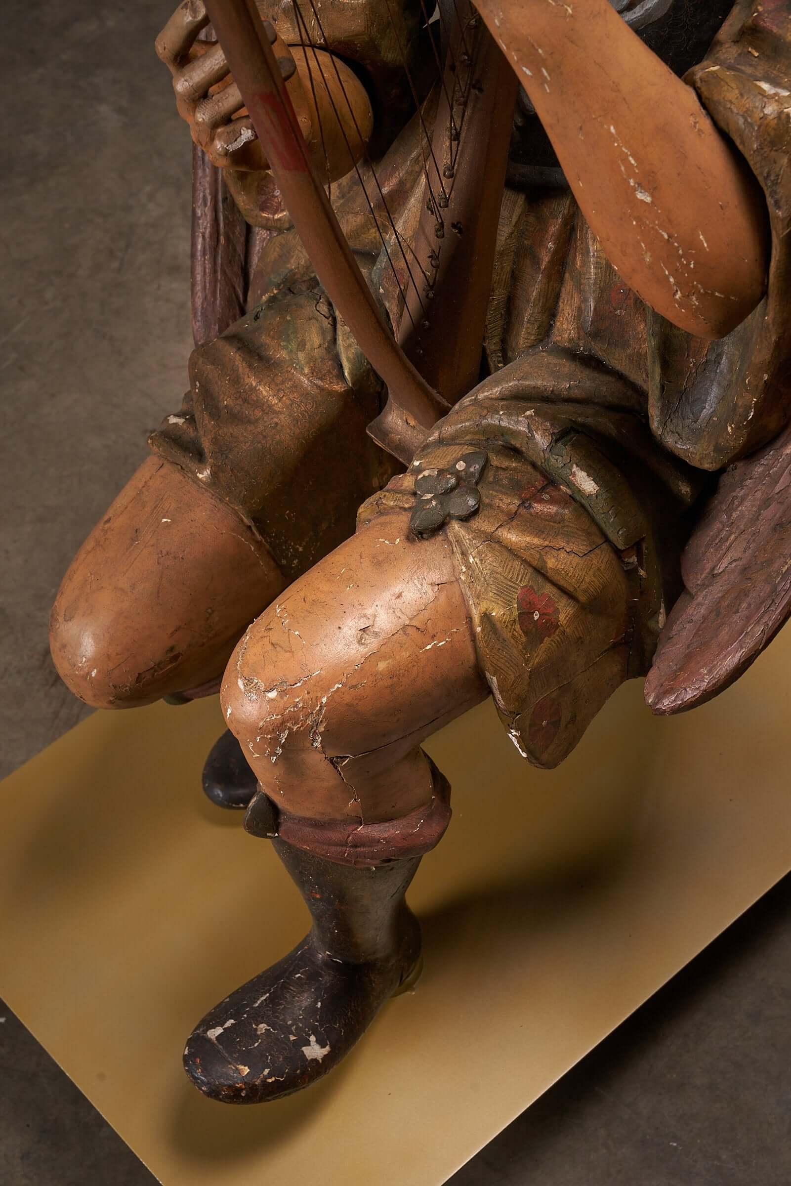 Detailed view of an antique hand-painted wooden angel sculpture playing a harp, showcasing 19th-century religious art details.