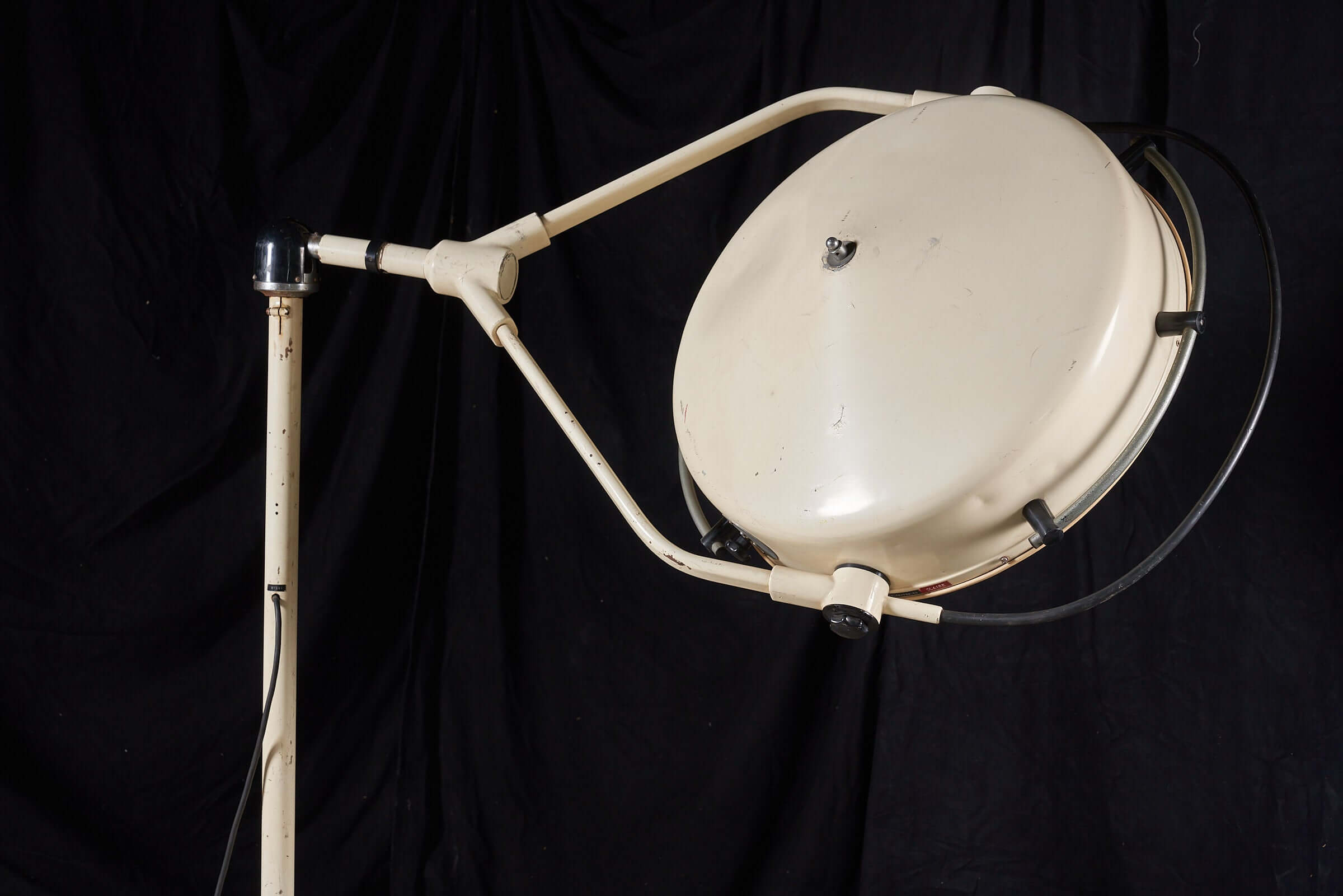 Vintage cream medical lamp by Chromophare with adjustable stand and large circular light on a black background.