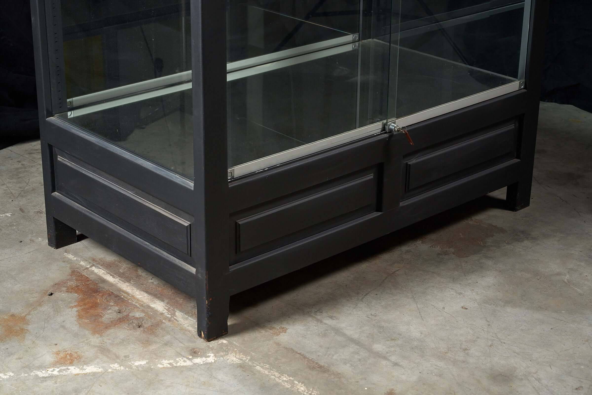 Close-up of the base of a vintage black display cabinet with glass panels and a sturdy frame.