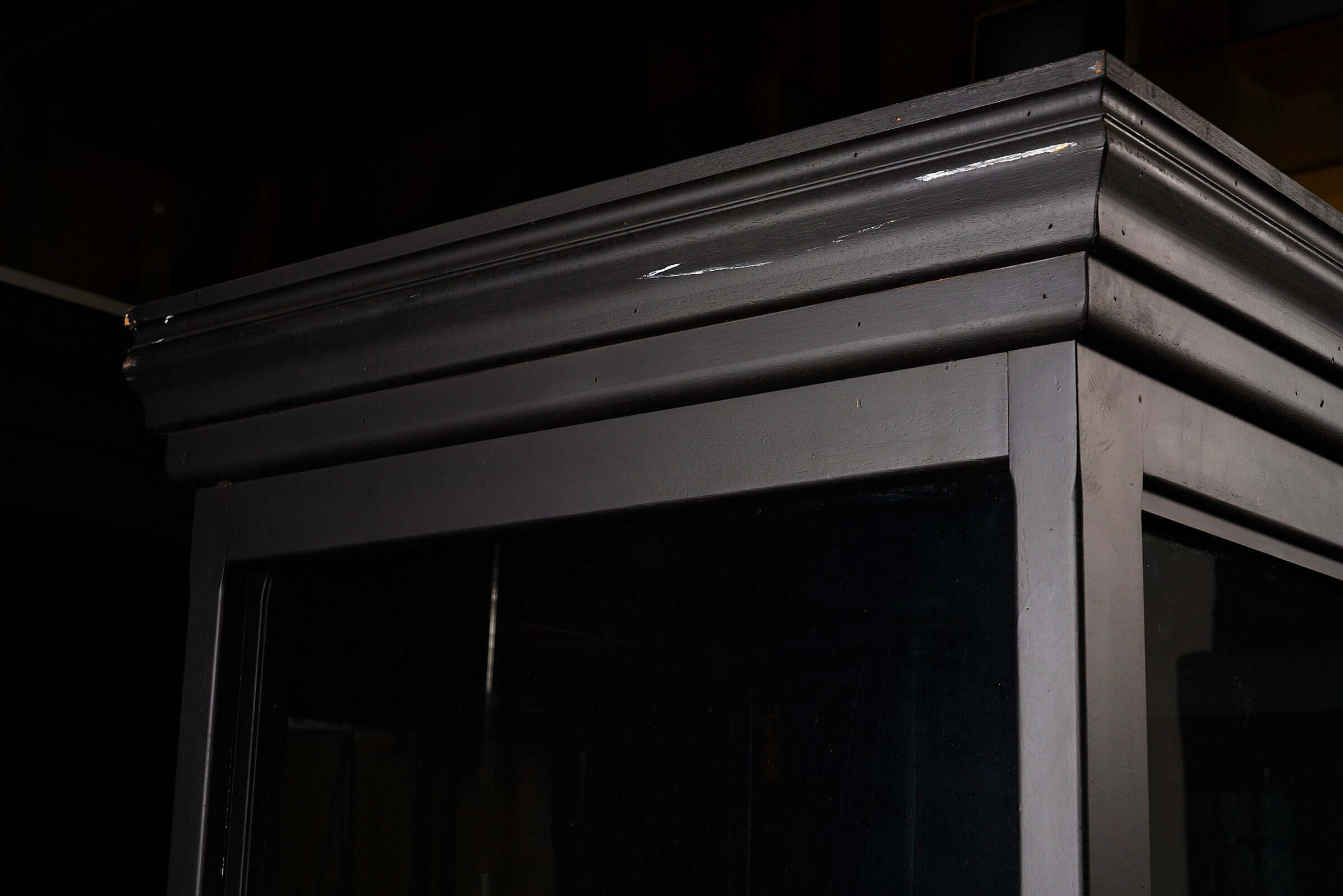 Close-up view of the top corner of a vintage black display cabinet with glass panels and a sleek finish