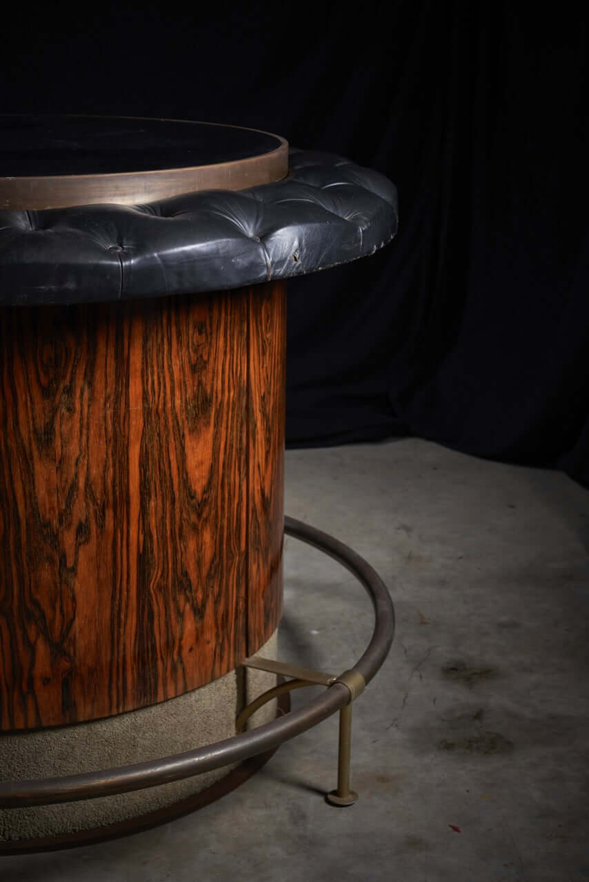 Vintage rosewood bar table with black leather tufted top and metal base, showcasing mid-century sophistication and retro charm.