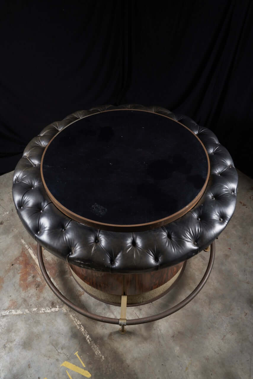 Vintage rosewood bar table with black leather tufted top and metal base, showcasing mid-century elegance and retro charm.