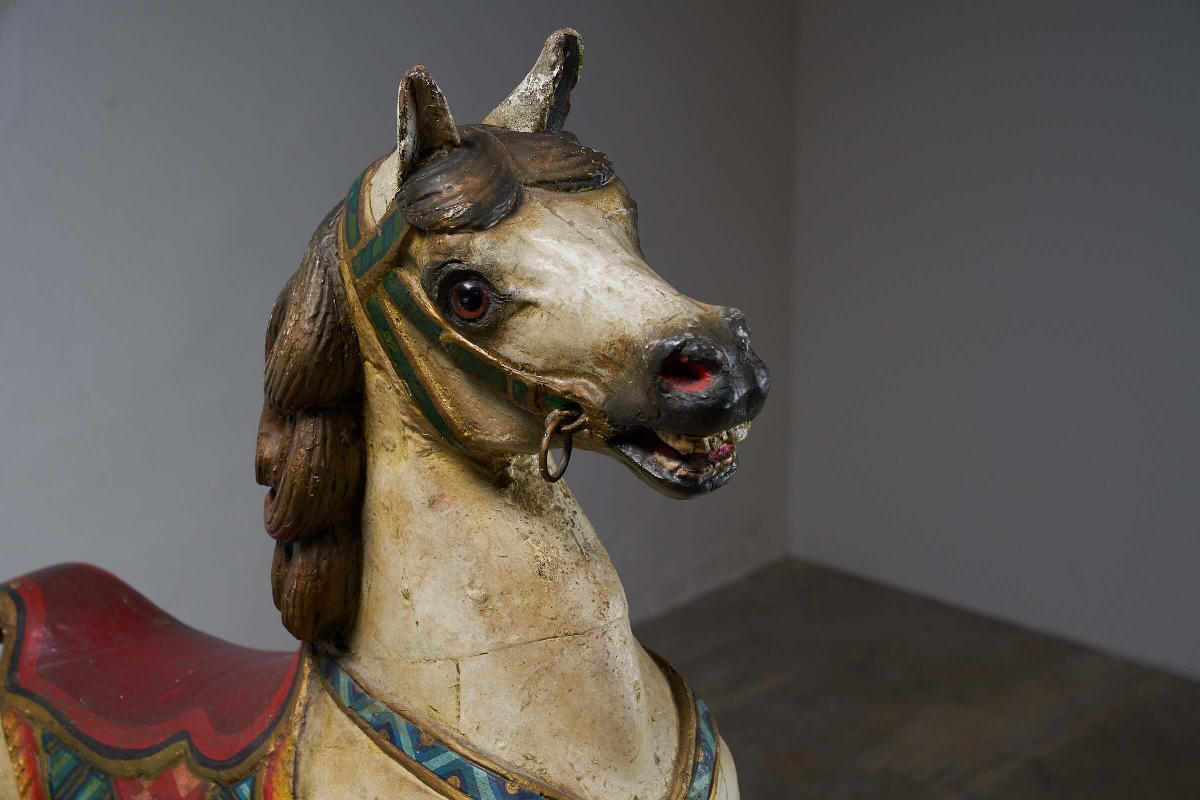 Close-up of antique hand-painted wooden carousel horse head with multicolored saddle and vibrant harness.