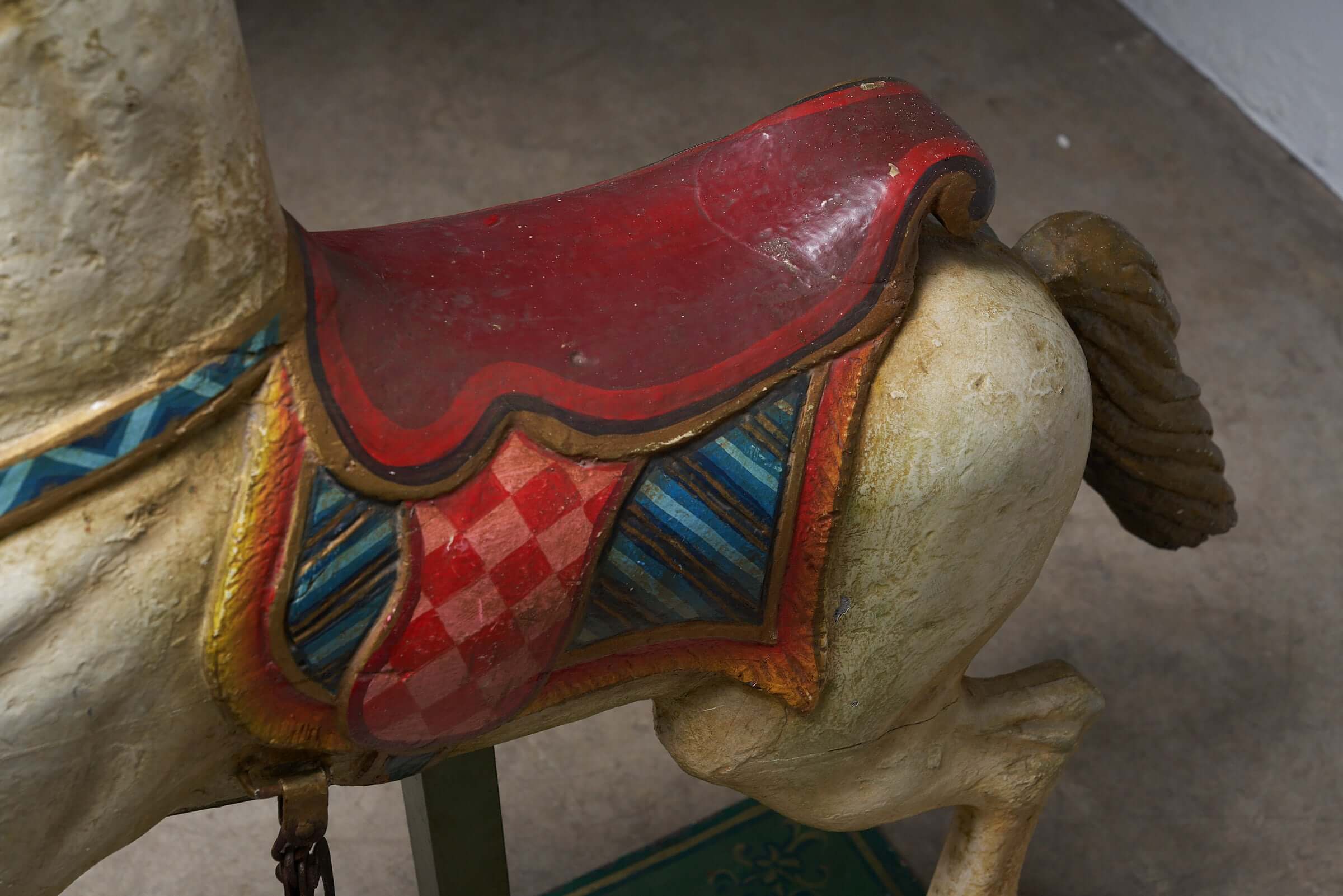 Close-up of vintage hand-painted wooden carousel horse with red saddle and multicolored harness detailing.