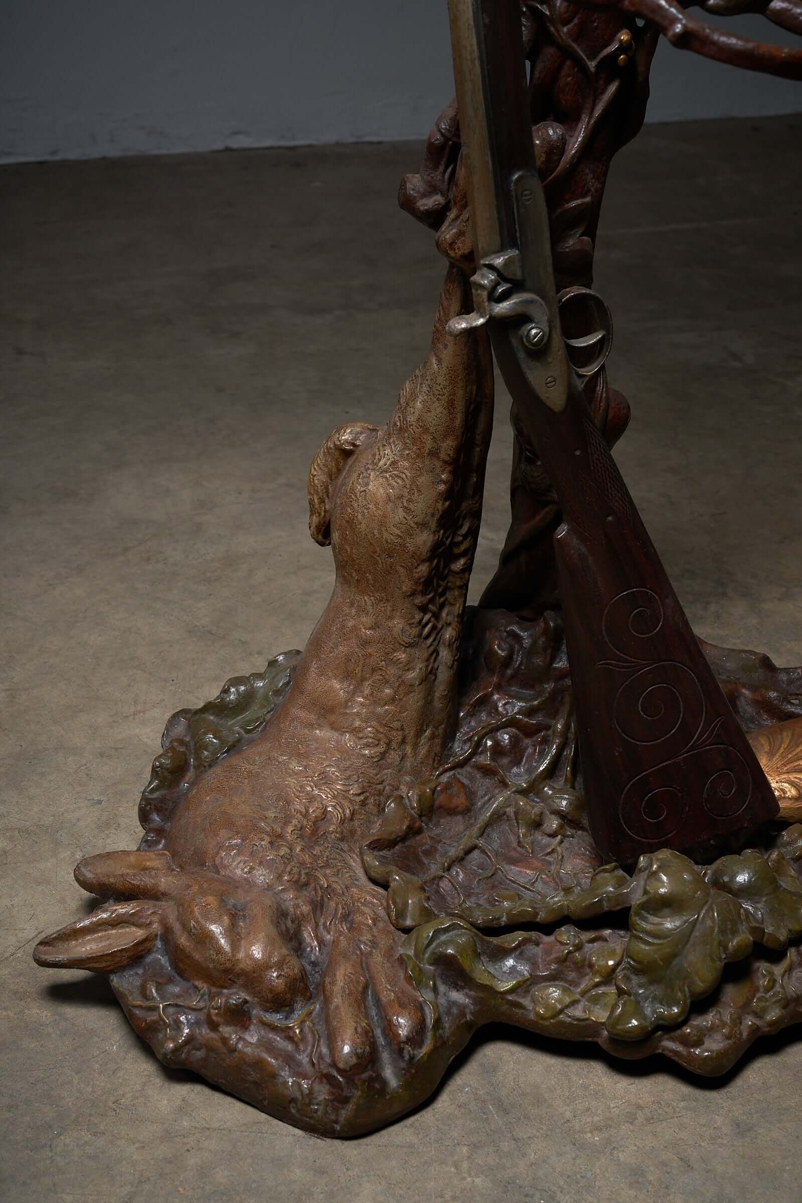 Detailed view of ornate iron hallway piece with hunting theme, featuring a sculpted rabbit and rifle in brown and gold accents.